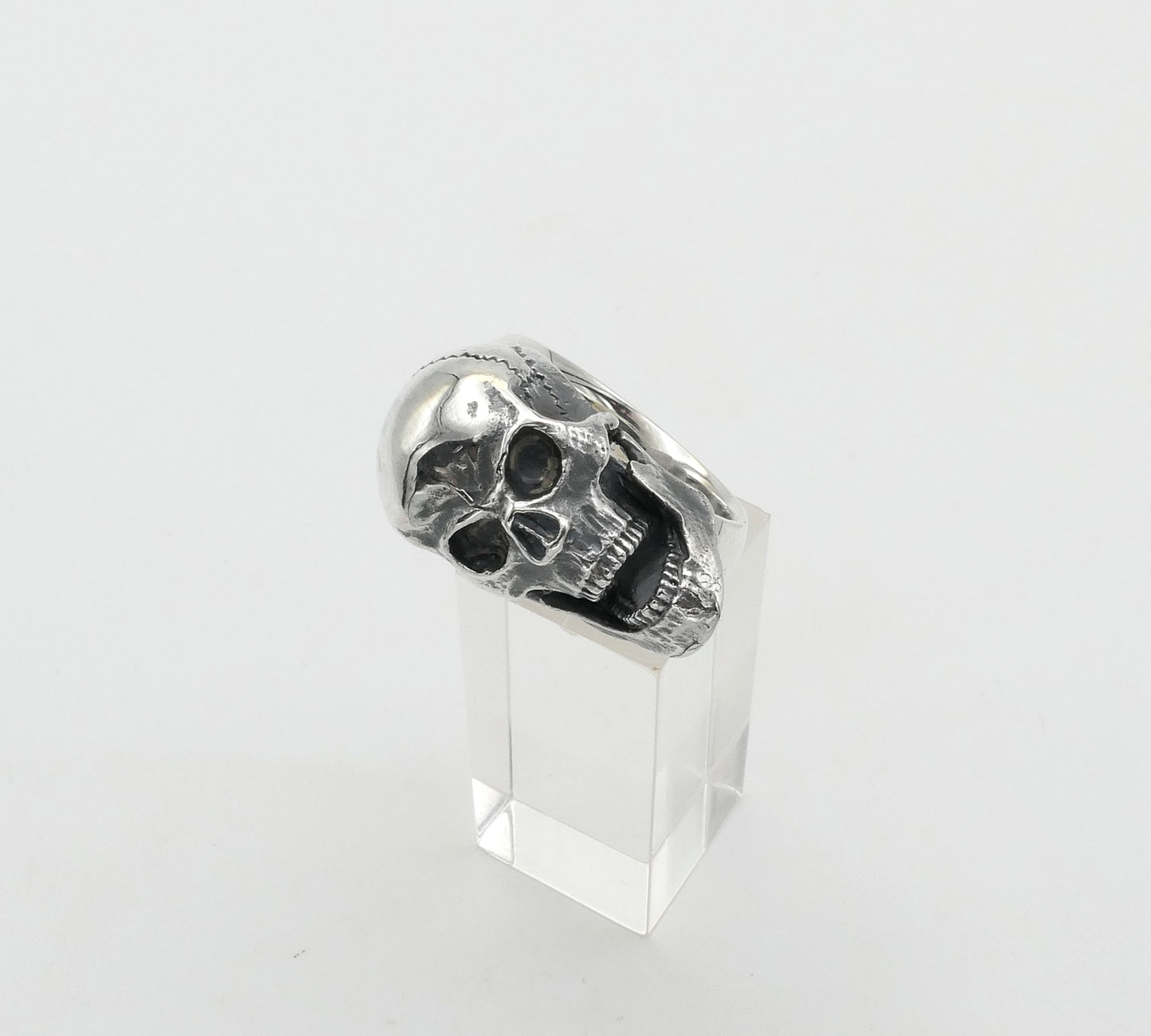 Silver skull ring on a clear stand against a white background
