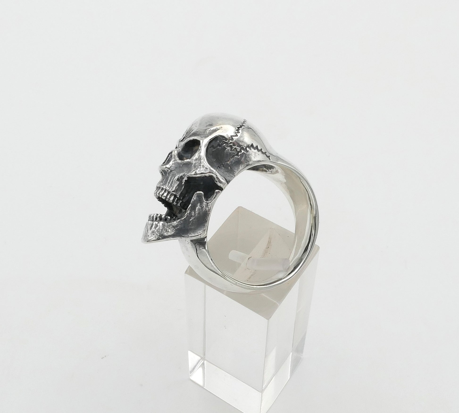 Silver skull ring on a clear stand against a white background