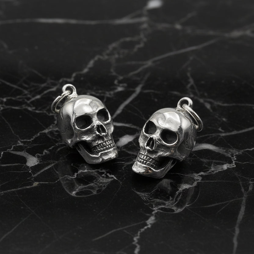 Two silver skull-shaped pendants on a light gray background