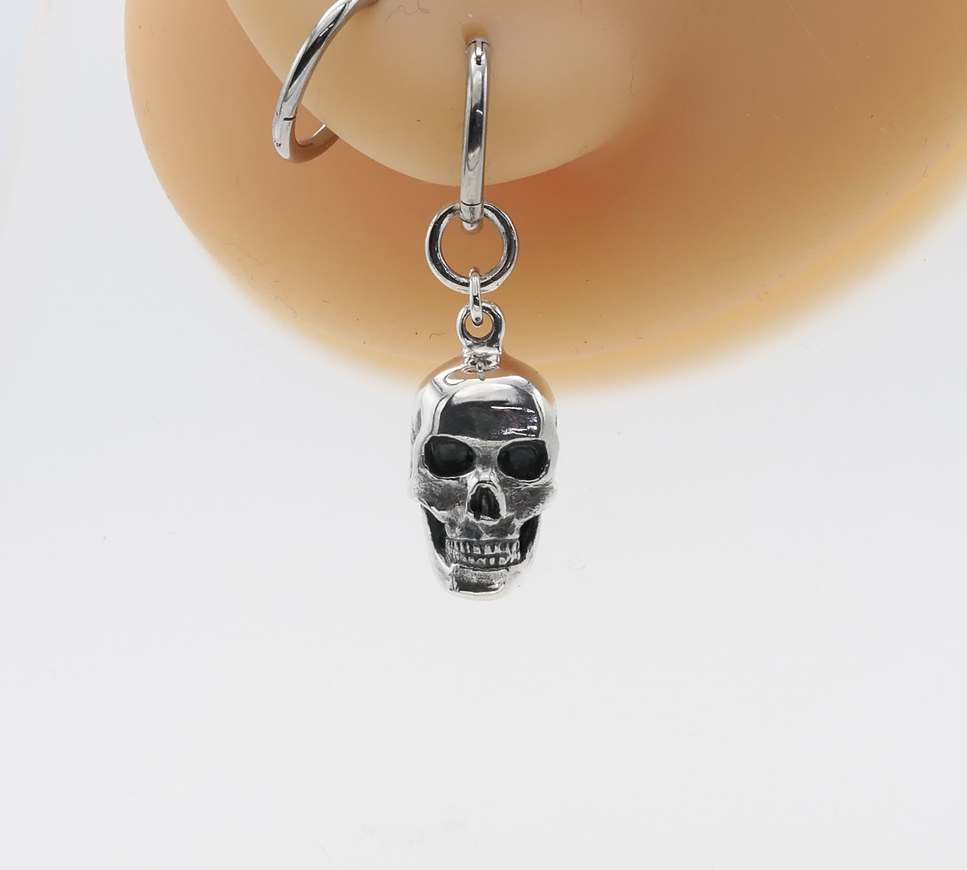 Silver skull-shaped earring on a white background