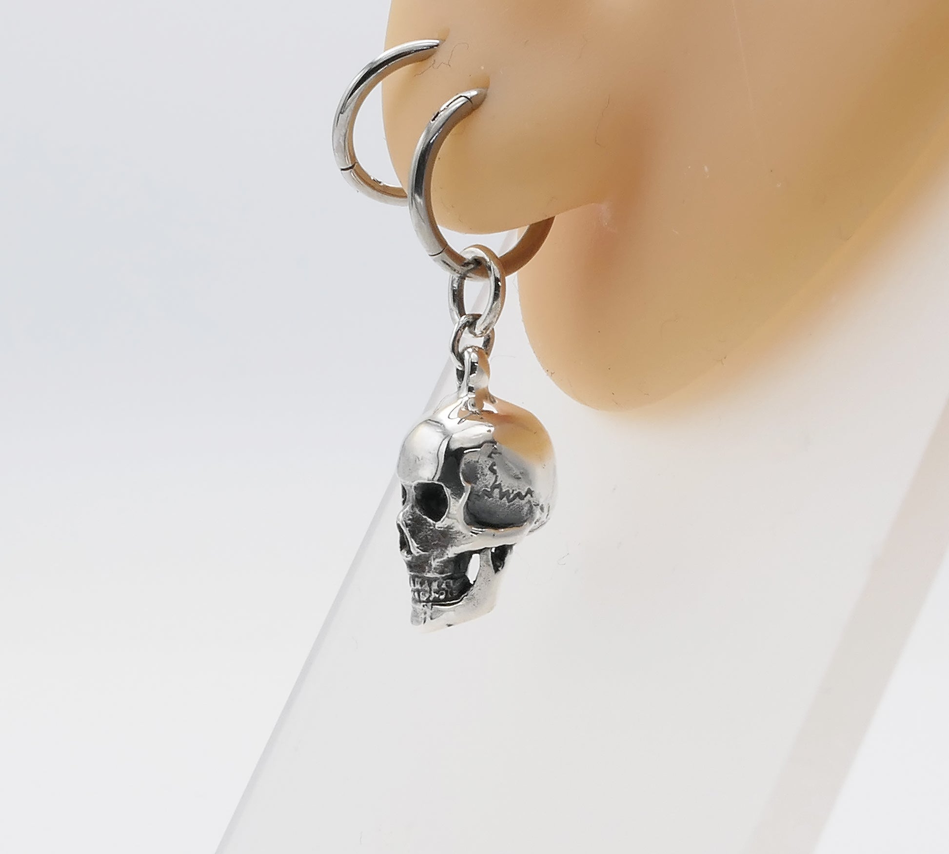 Silver skull earring on a mannequin ear with a white background