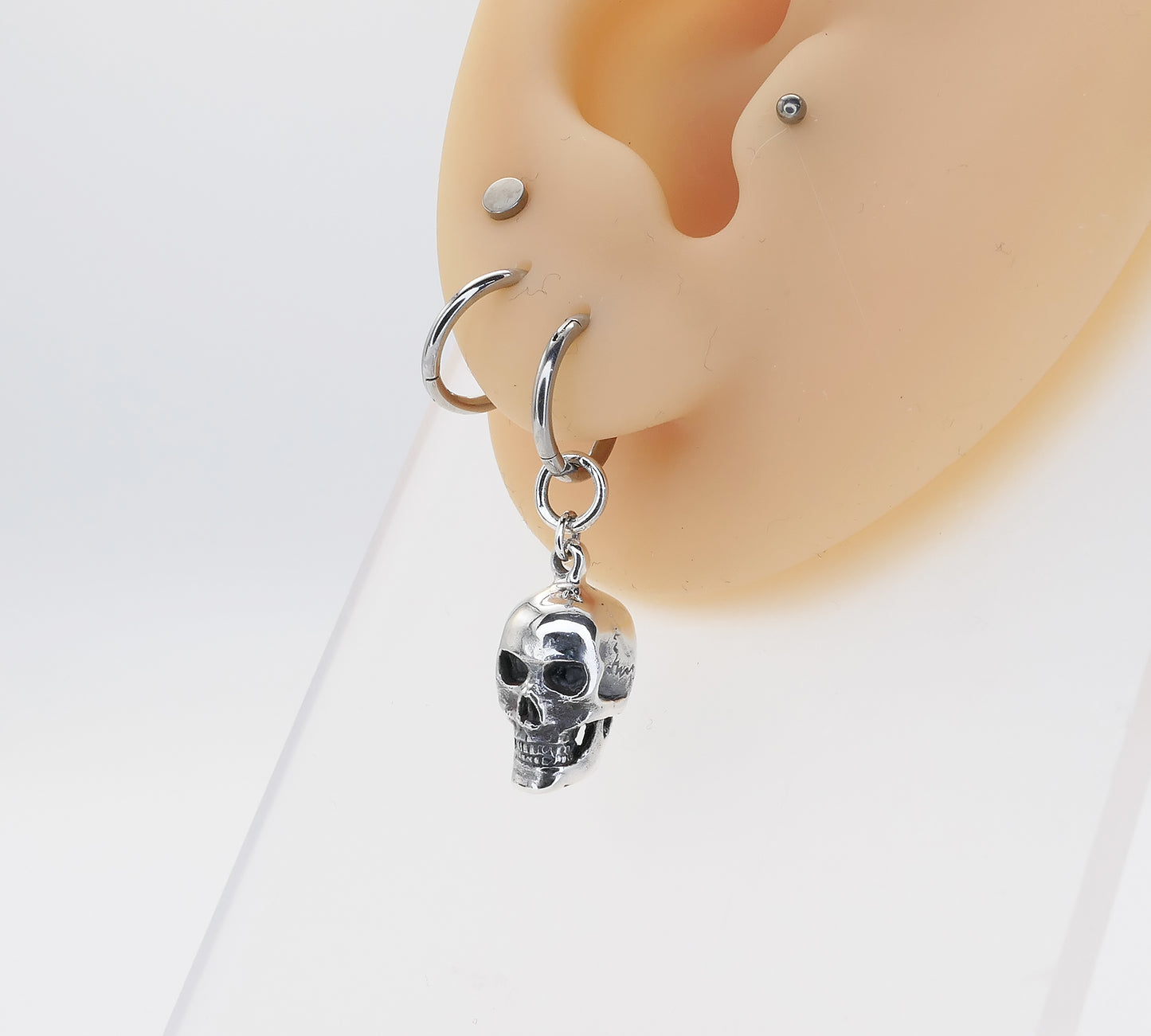 Silver skull-shaped earring on a mannequin ear with a white background