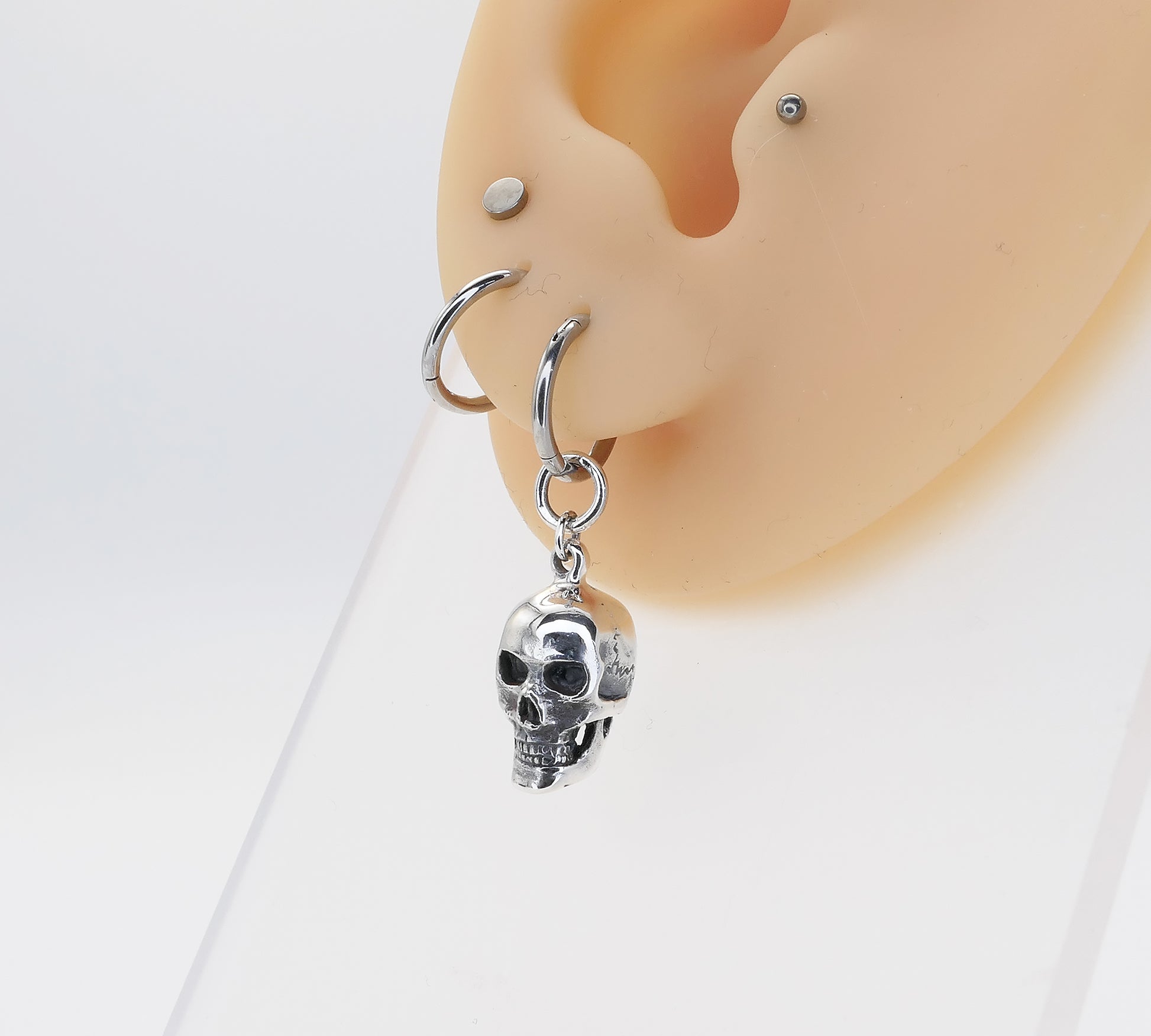 Silver skull-shaped earring on a mannequin ear with a white background