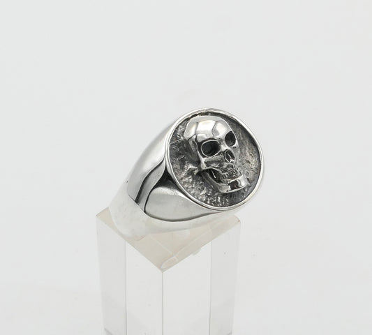 Silver skull signet ring on a clear stand against a light gray background