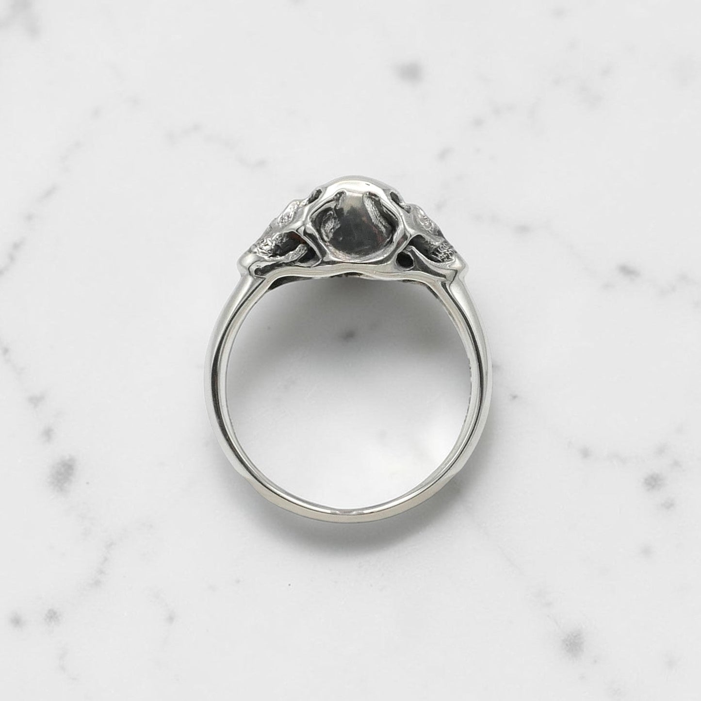 Sterling silver ring with twin skull design displayed on a clear stand against a black background.