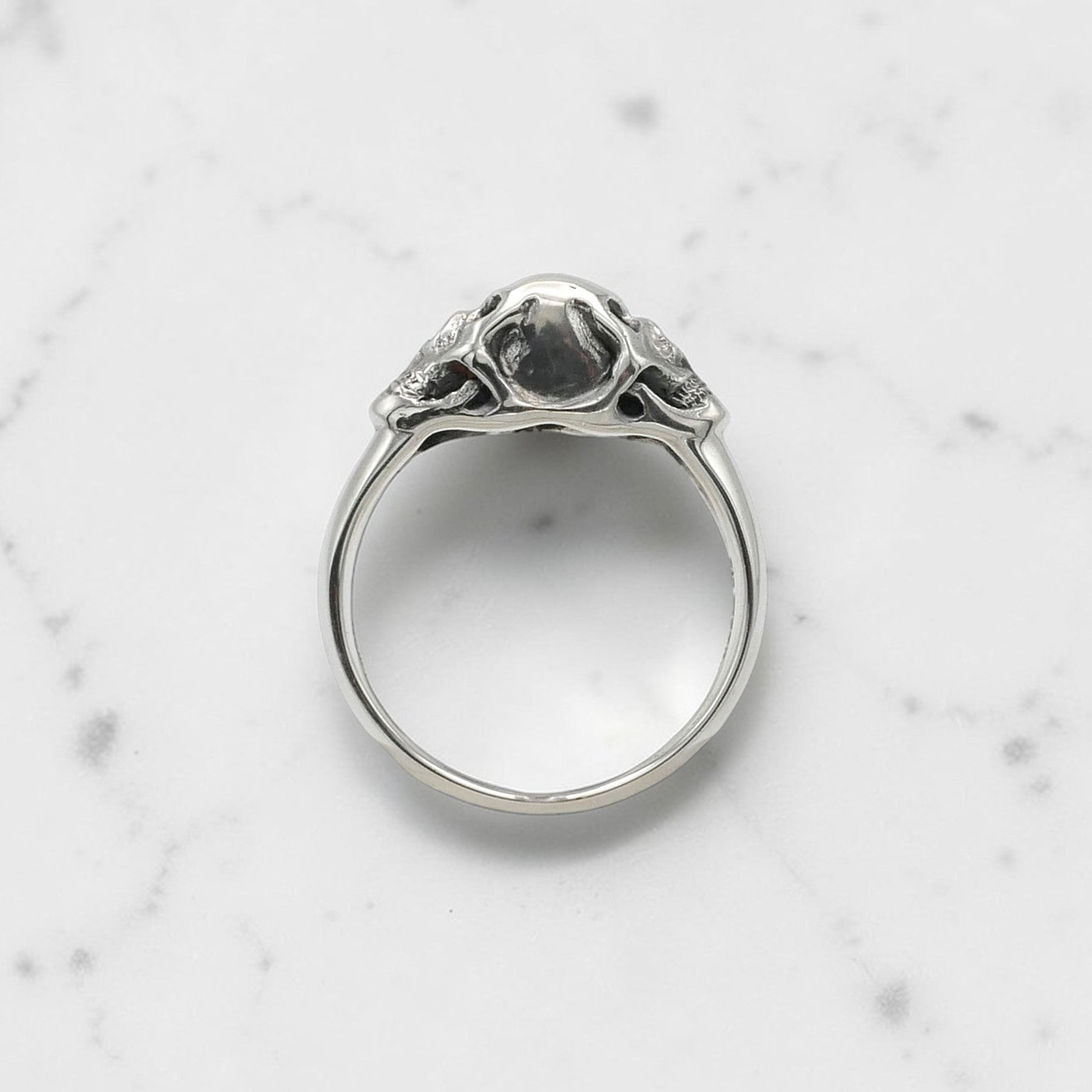 Sterling silver ring with twin skull design displayed on a clear stand against a black background.