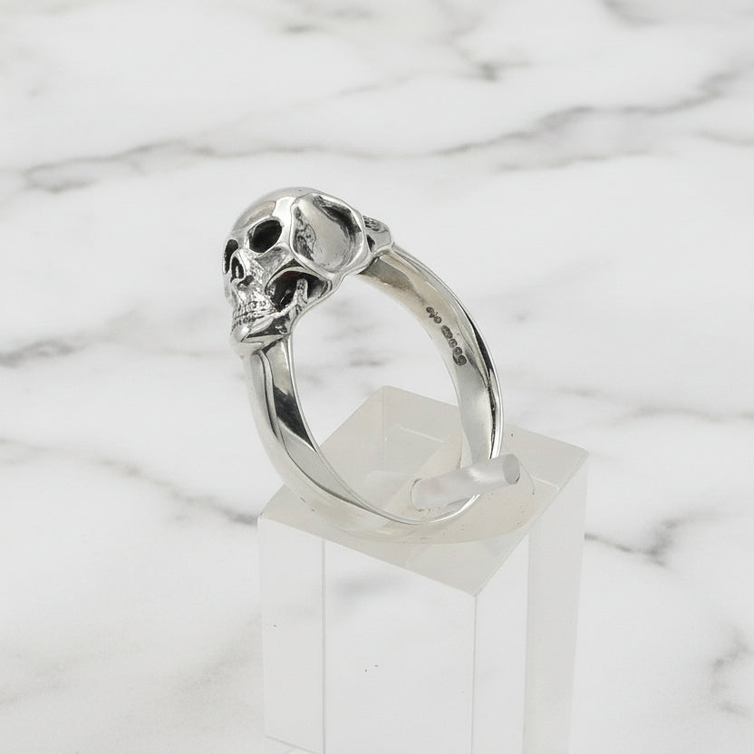Silver skull ring on a clear stand against a white background