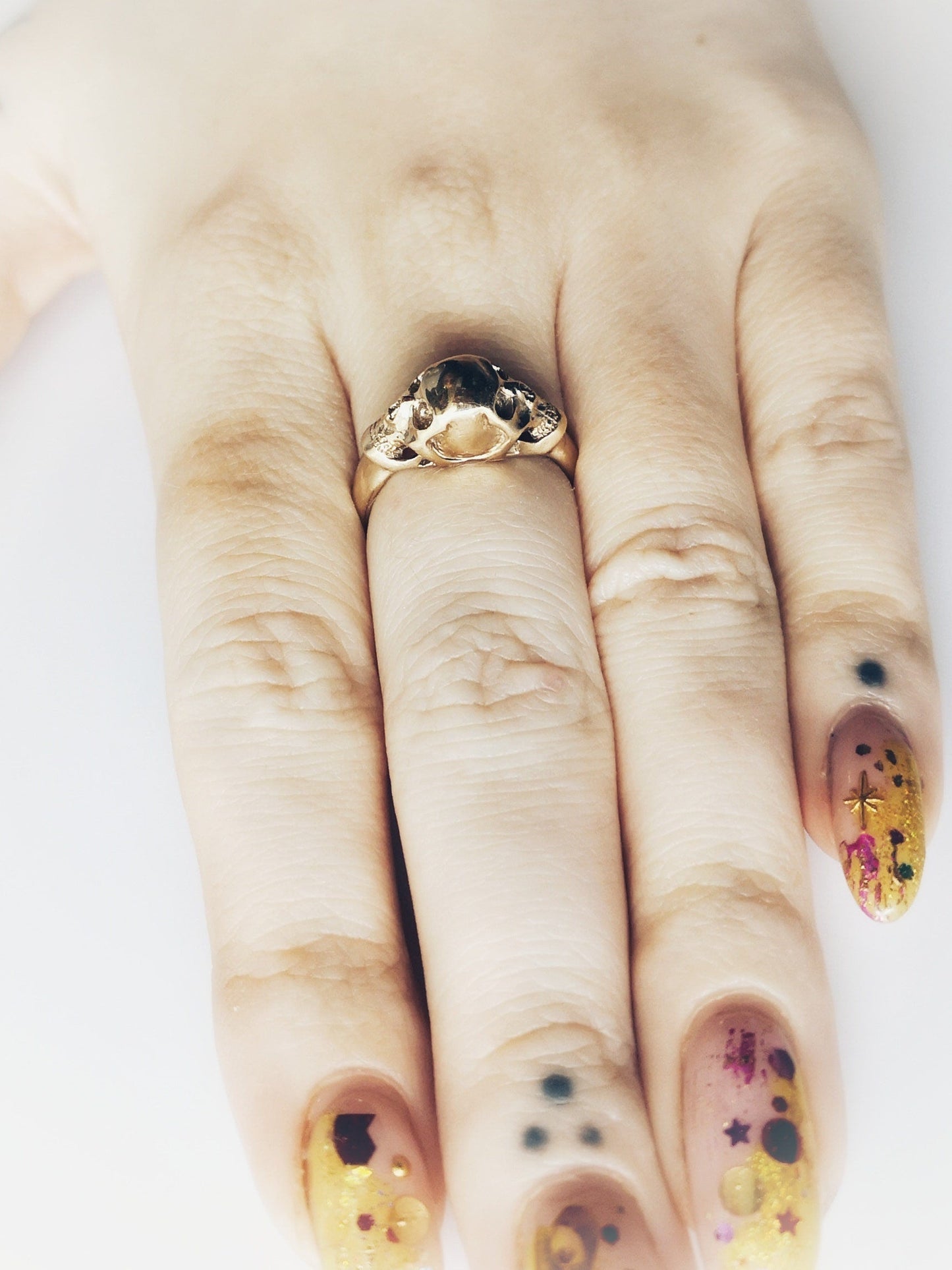 Hand wearing a gold ring with decorative nail art on a white background