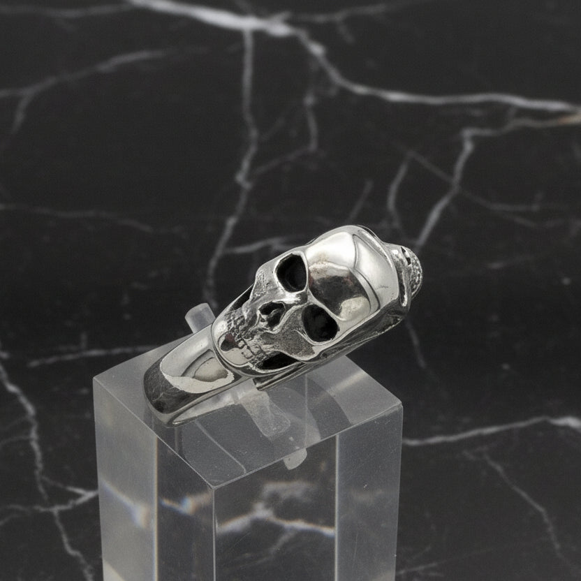 Silver skull ring on a clear stand against a white background