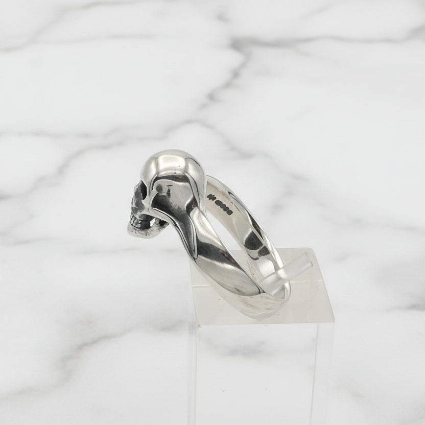 Silver skull ring on a clear stand against a white background