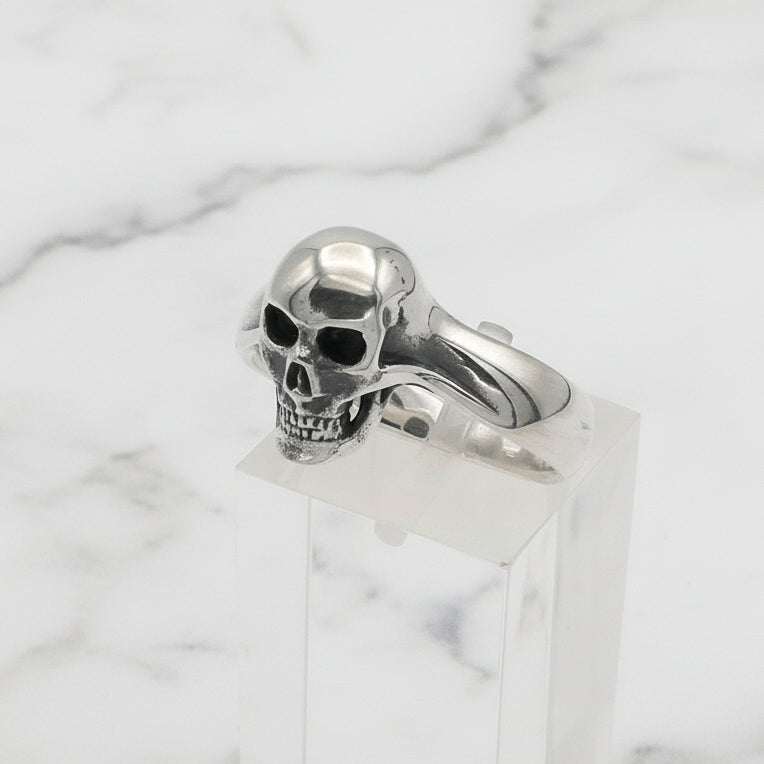 Silver skull ring on a clear stand against a white background