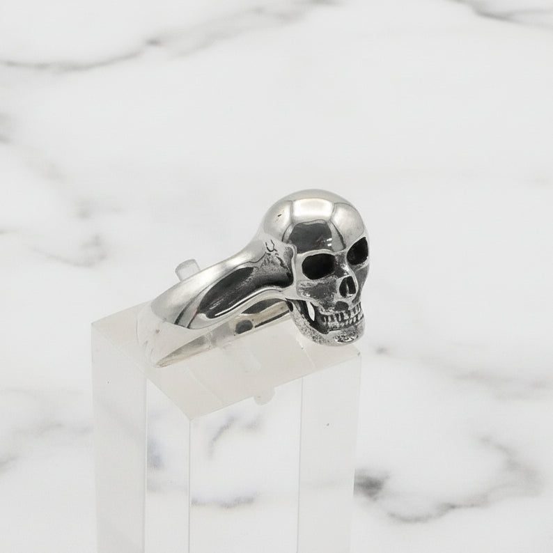 Silver skull ring on a clear stand with a white background
