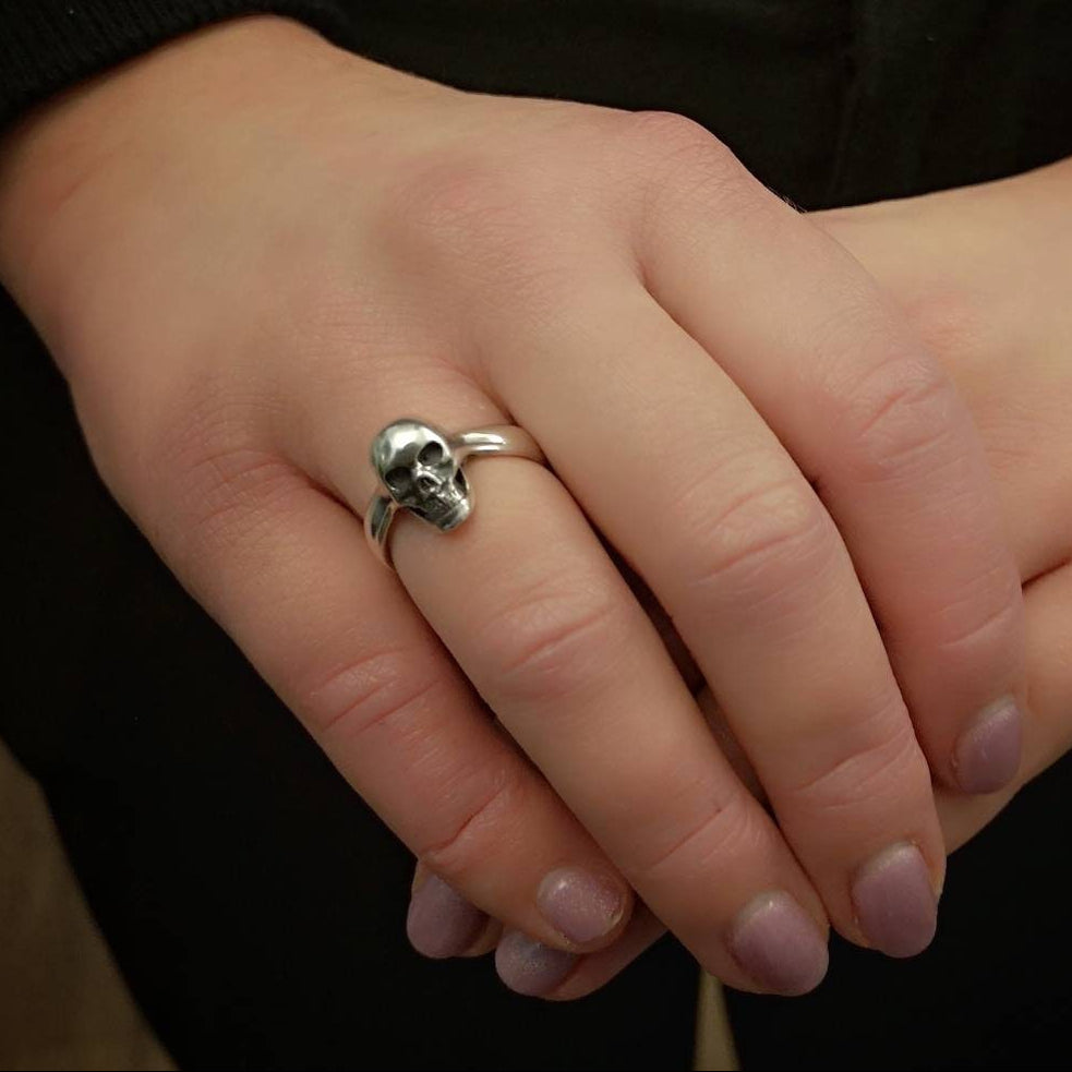 Silver skull ring on a person's finger against a dark background
