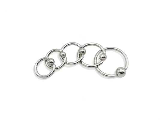 A collection of surgical steel ball closure rings in various sizes, with a polished metallic finish.