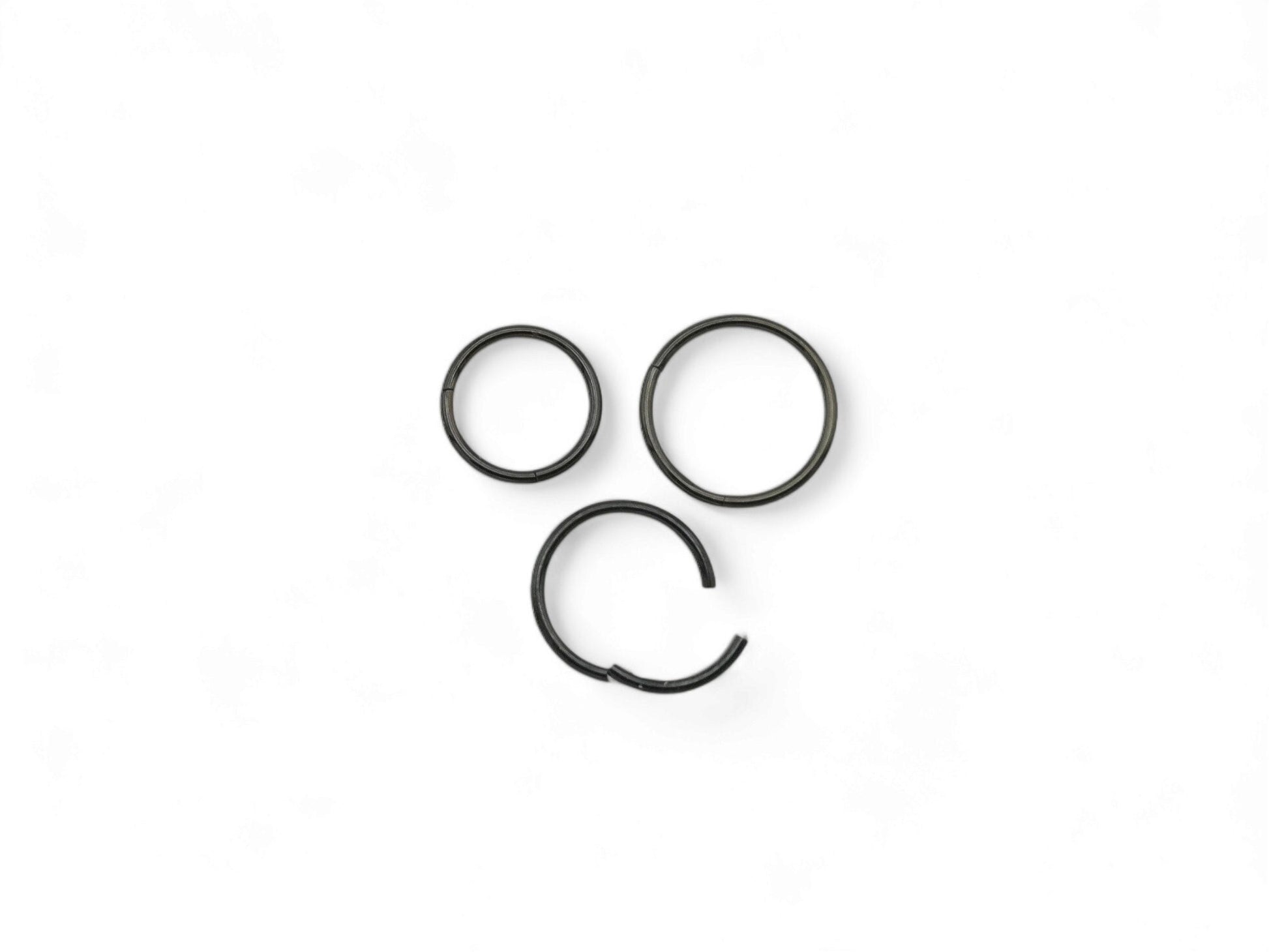 Three black surgical steel clicker rings for nose piercings, placed against a white background.