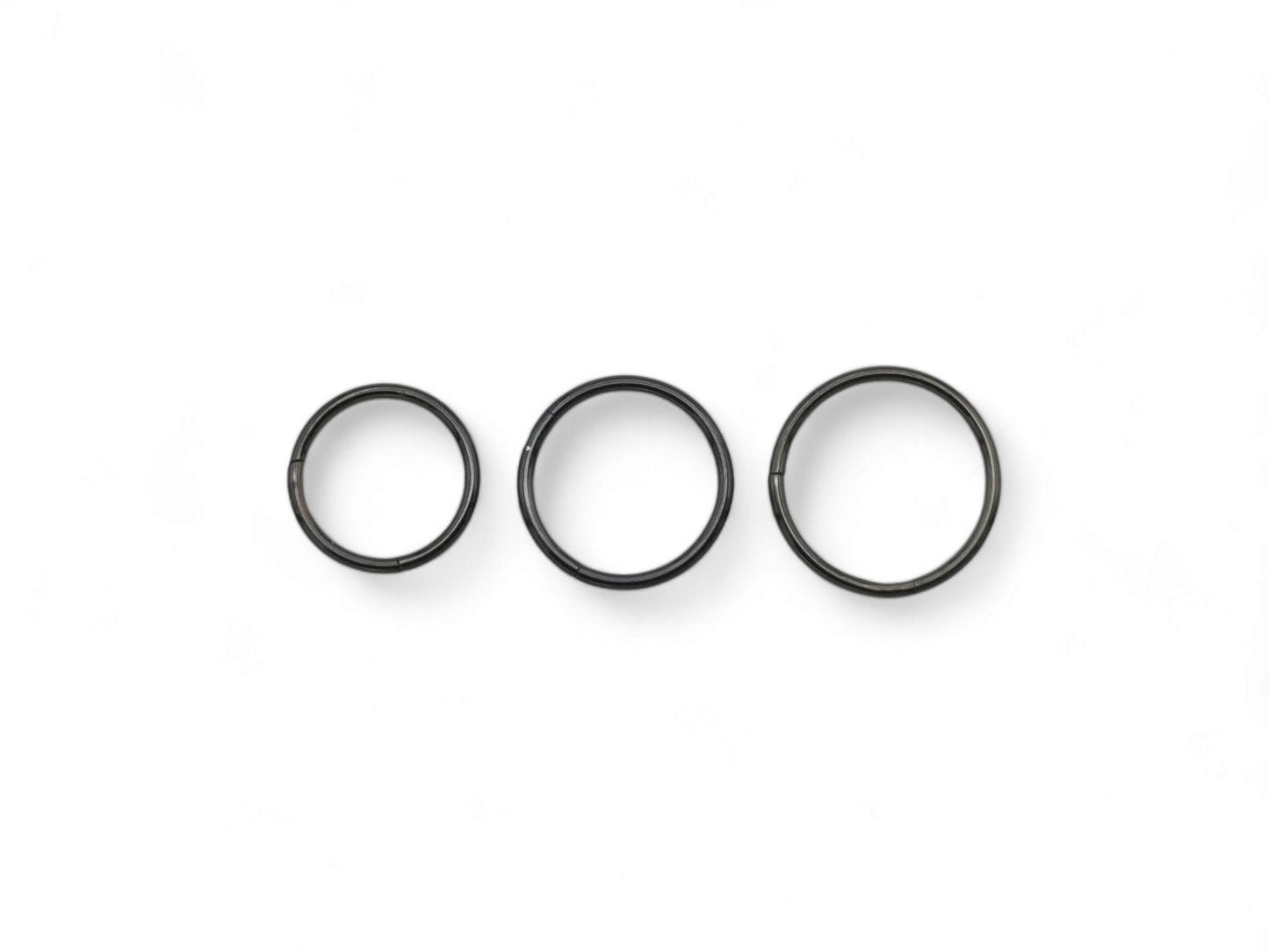 Three black surgical steel clicker rings for nose piercings, placed against a white background.