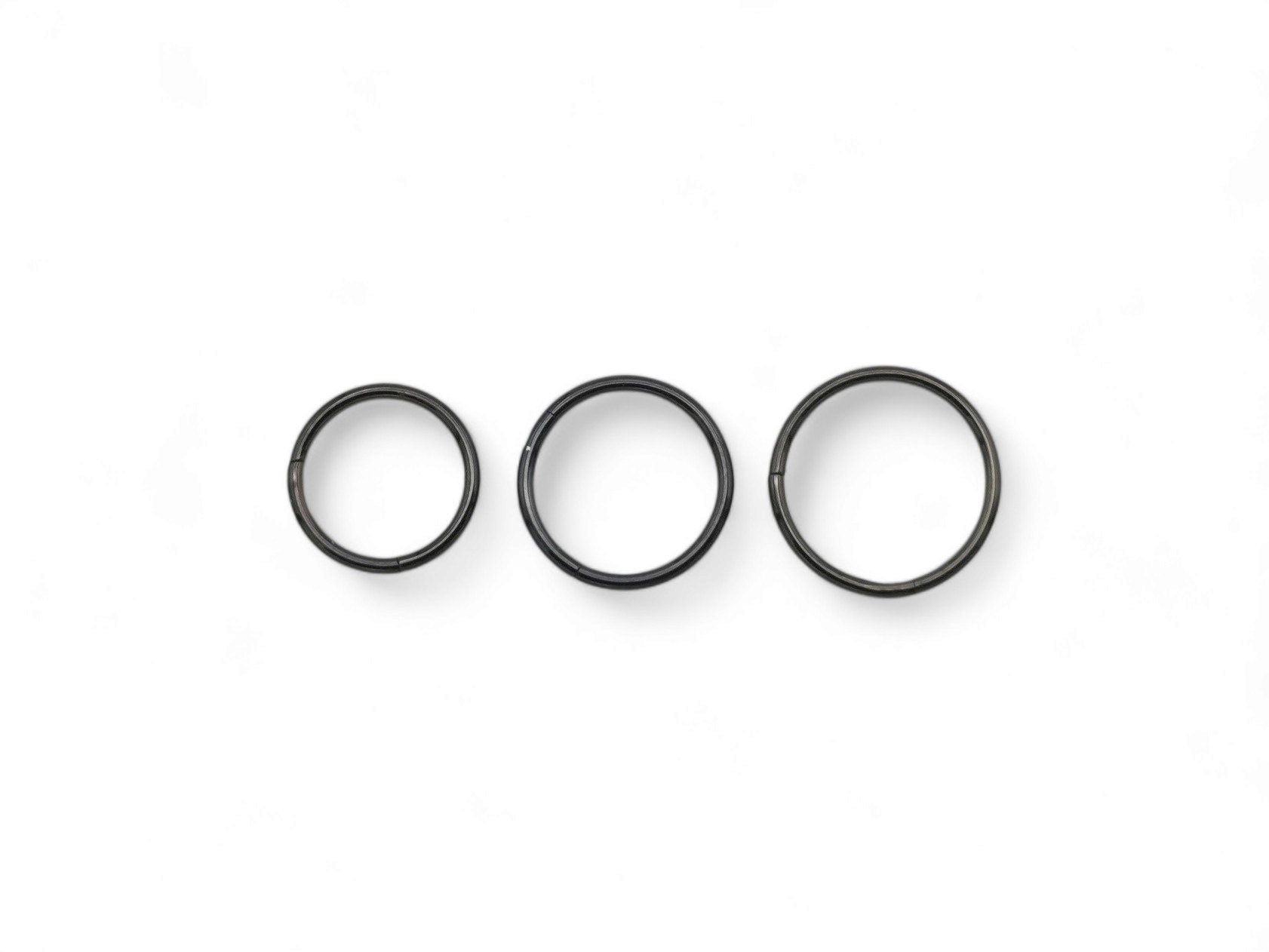 Three black surgical steel clicker rings for nose piercings, placed against a white background.