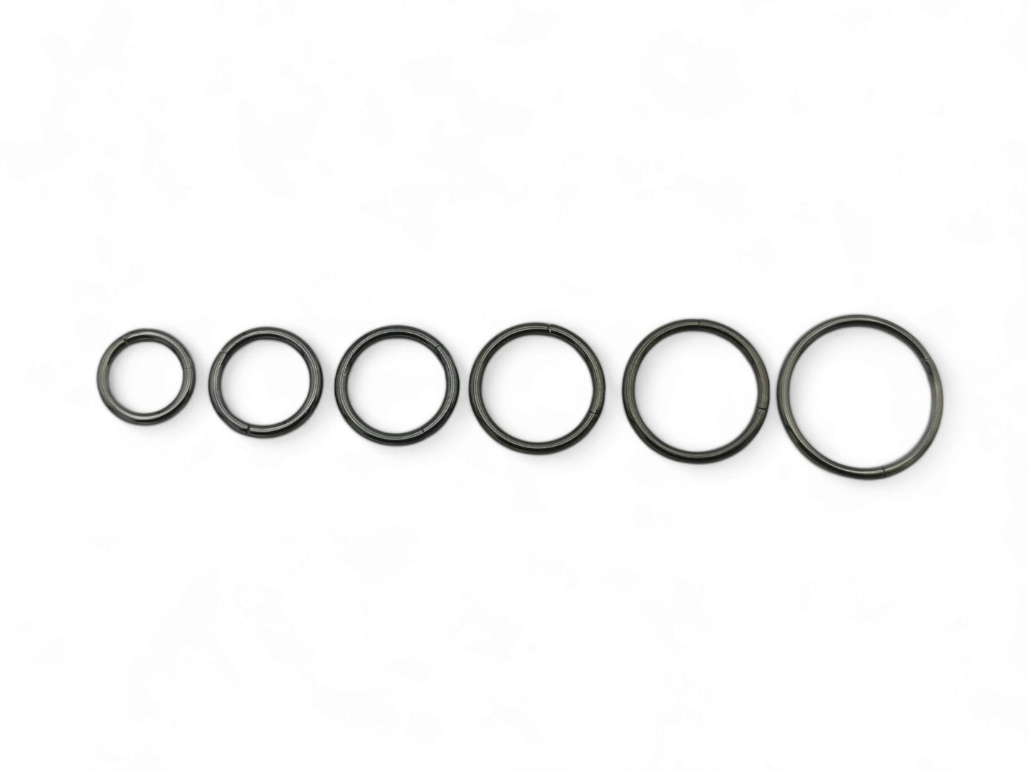A set of six black surgical steel clicker rings arranged in parallel against a white background.