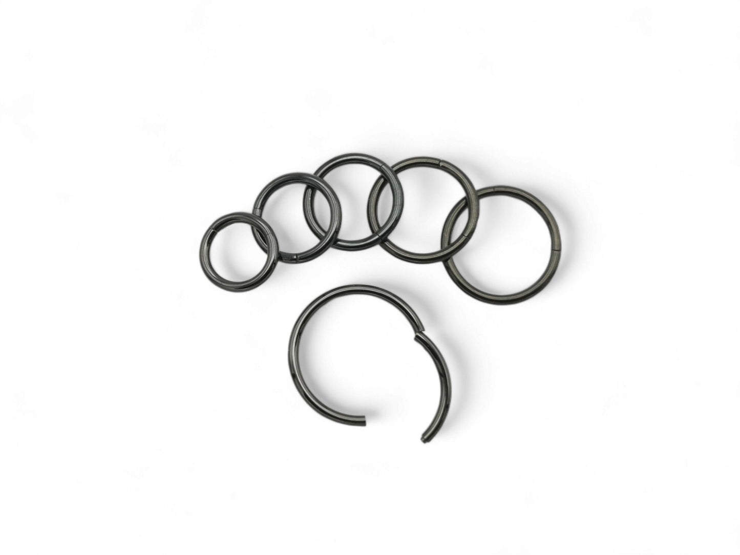 A set of six black surgical steel clicker rings arranged in parallel against a white background.