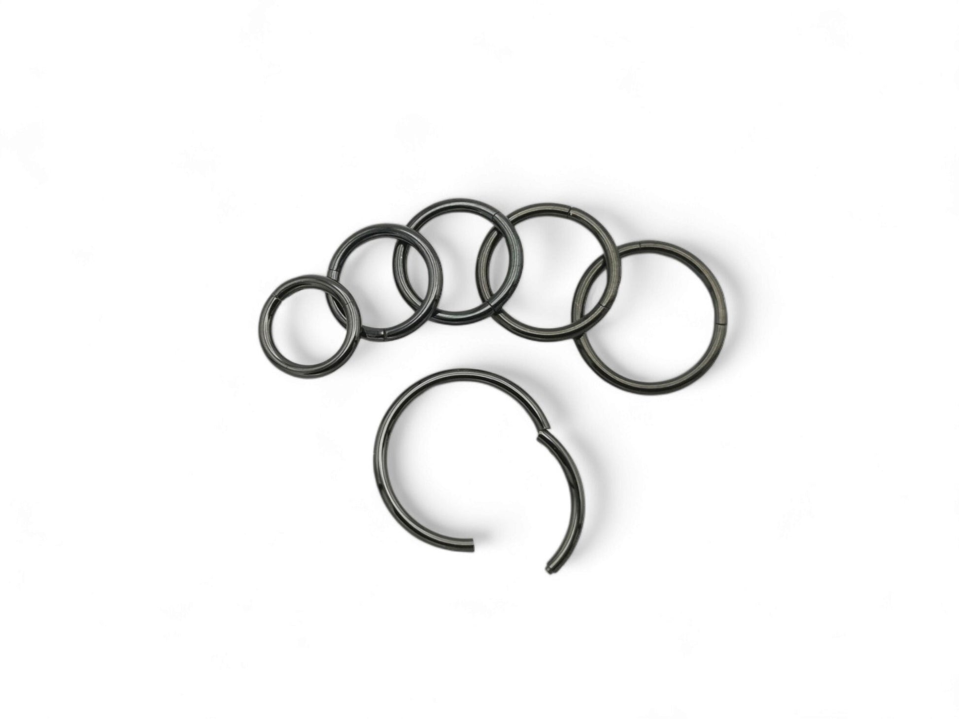 A set of six black surgical steel clicker rings arranged in parallel against a white background.