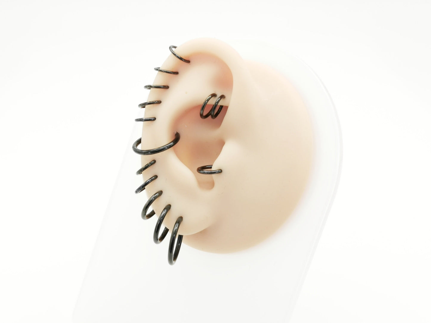A set of black surgical steel clicker rings arranged in parallel worn on a mannequin ear