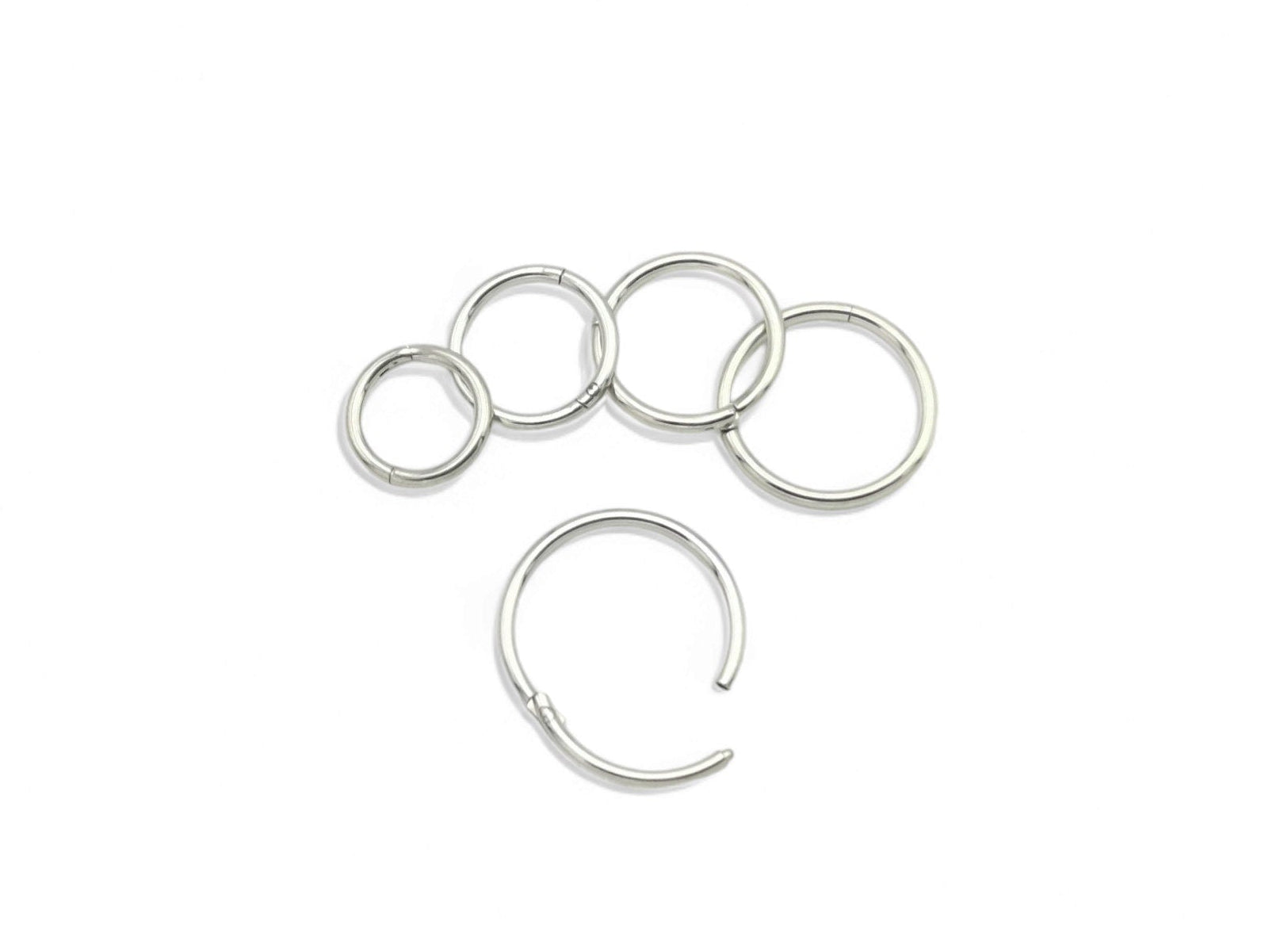 A set of five silver surgical steel clicker rings, with varying internal diameters for ear and nose piercings.