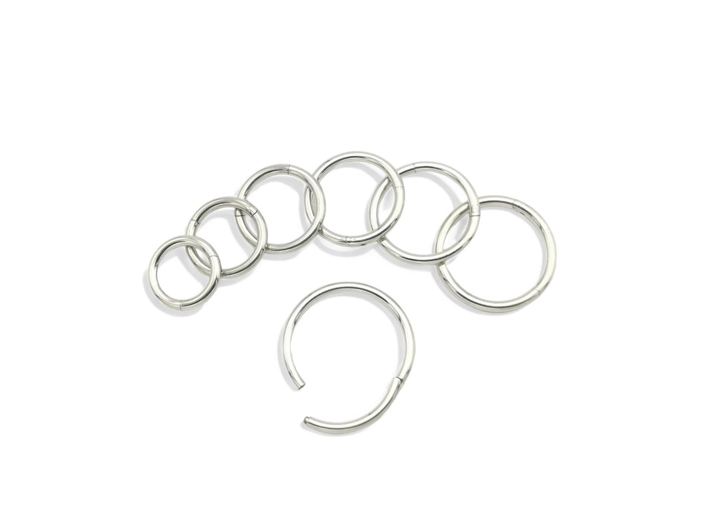 A set of seven surgical steel clicker rings, varying in size, displayed on a white background.