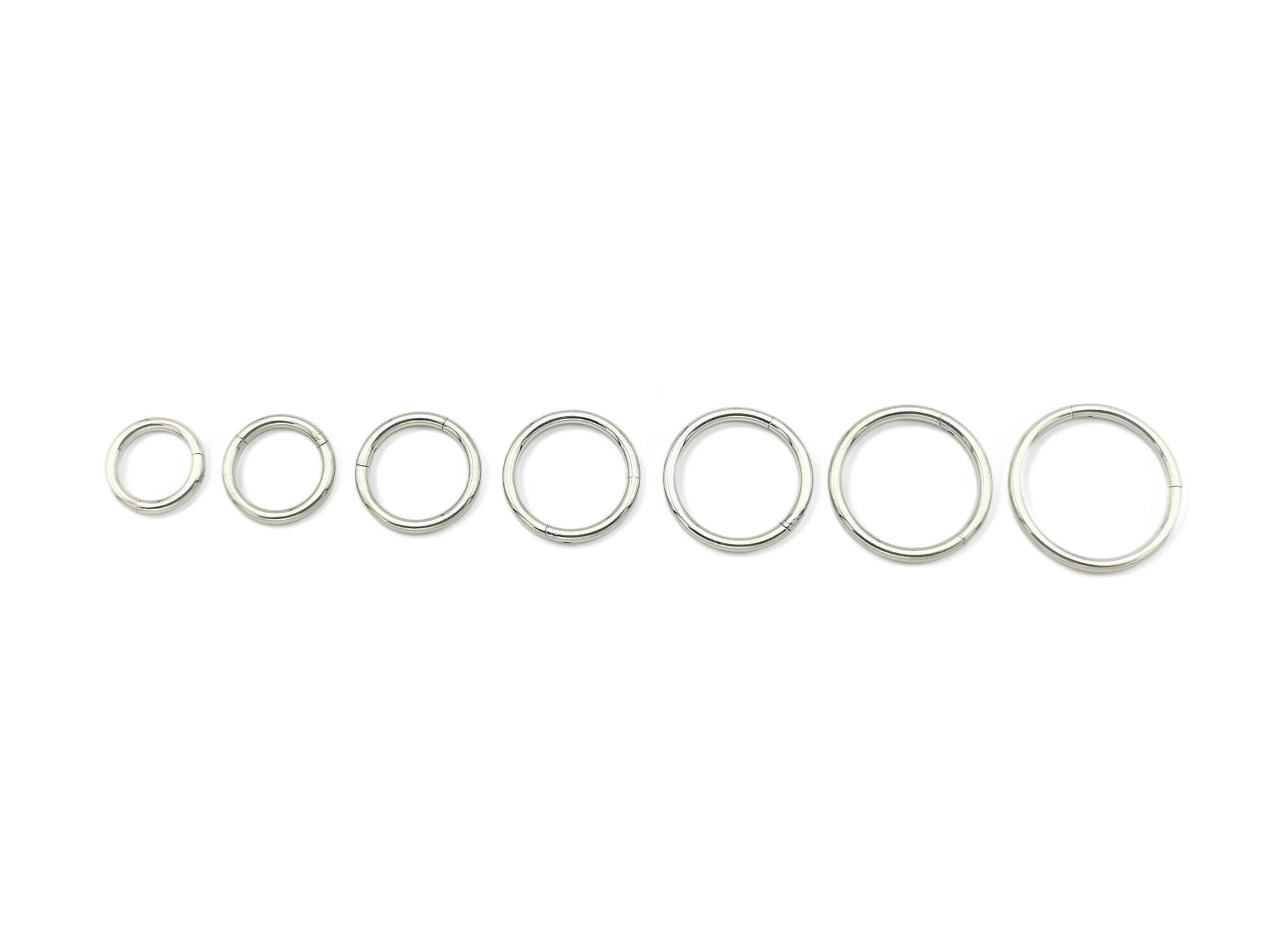 A set of seven surgical steel clicker rings, varying in size, displayed on a white background.
