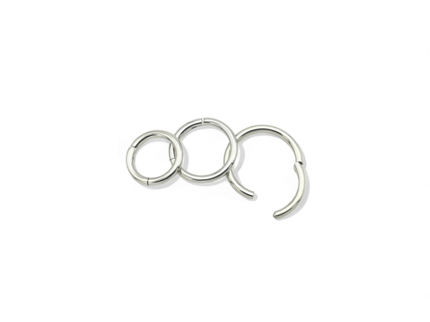A set of three surgical steel clicker rings in increasing sizes, arranged in a triangular formation, with a shiny metallic finish.