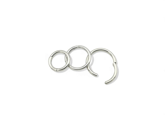 A set of three surgical steel clicker rings in increasing sizes, arranged in a triangular formation, with a shiny metallic finish.