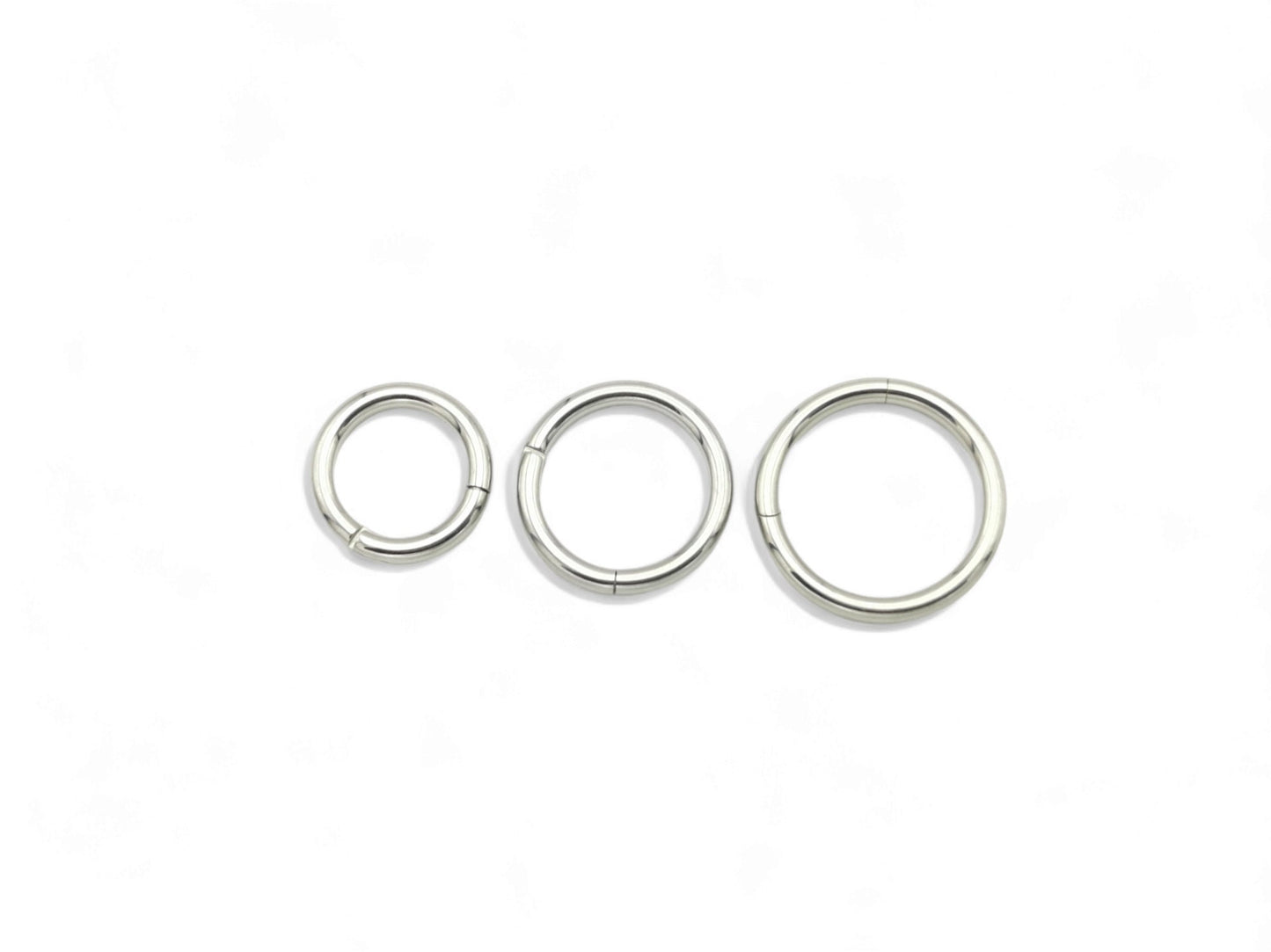 A set of three surgical steel clicker rings in increasing sizes, arranged in a triangular formation, with a shiny metallic finish.