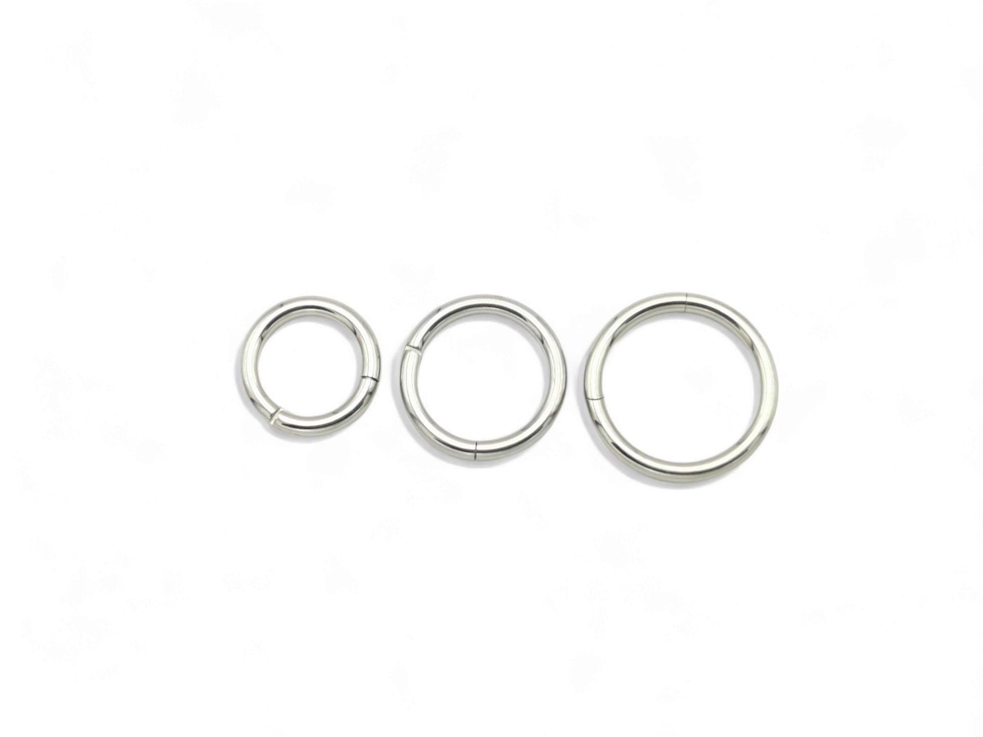 A set of three surgical steel clicker rings in increasing sizes, arranged in a triangular formation, with a shiny metallic finish.