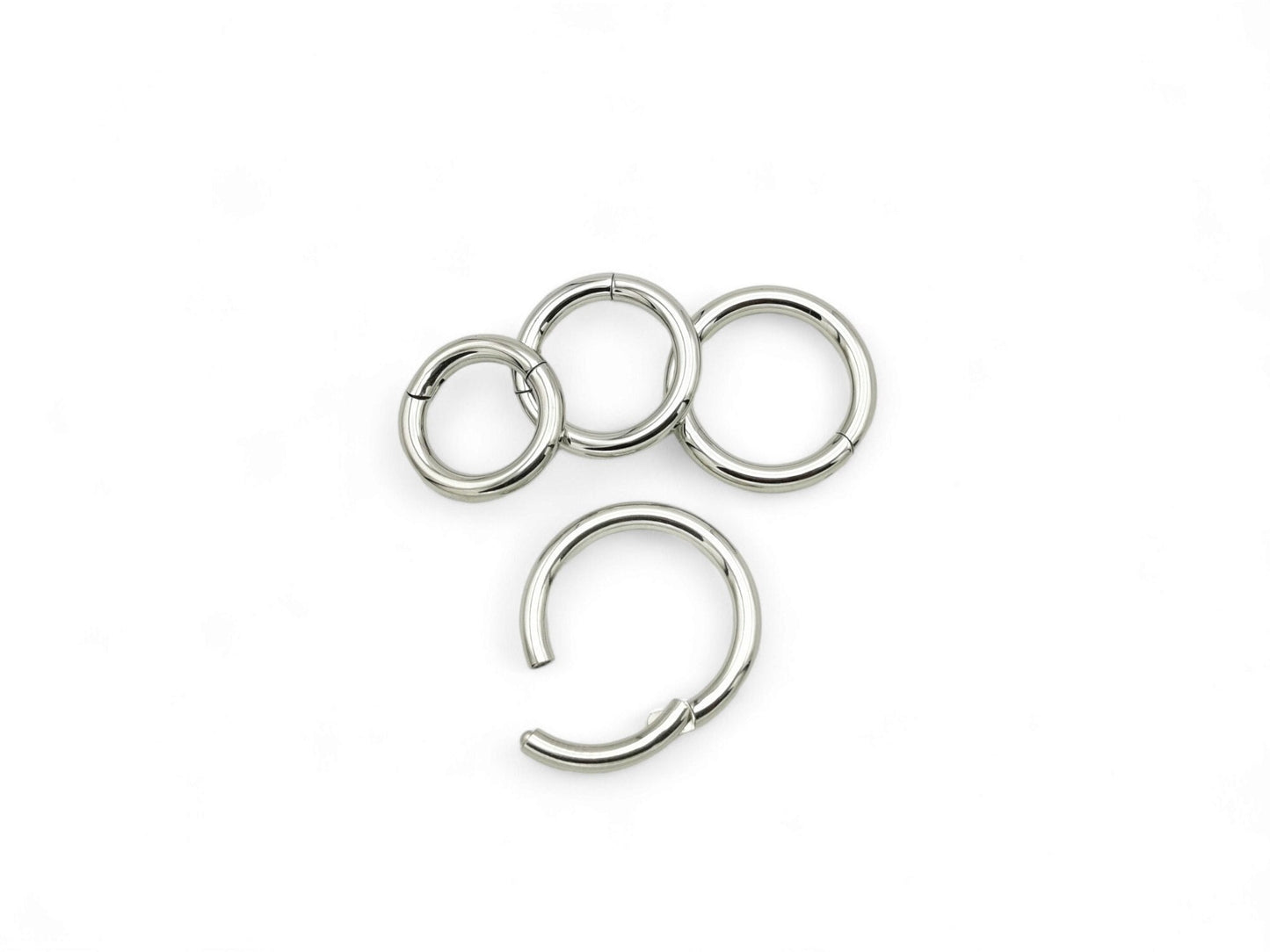 A set of four silver surgical steel clicker rings for body piercing, displayed on a white background.