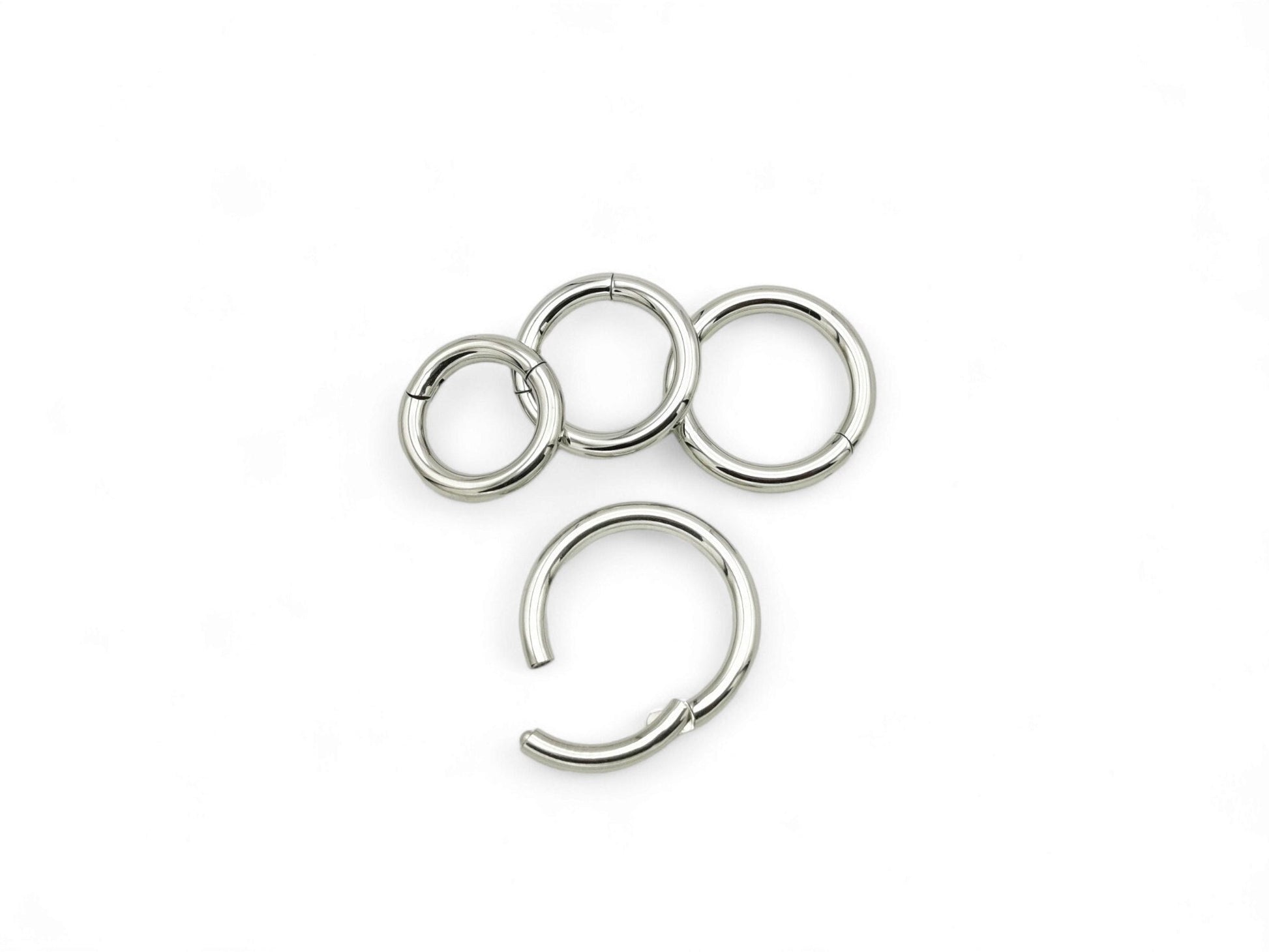 A set of four silver surgical steel clicker rings for body piercing, displayed on a white background.