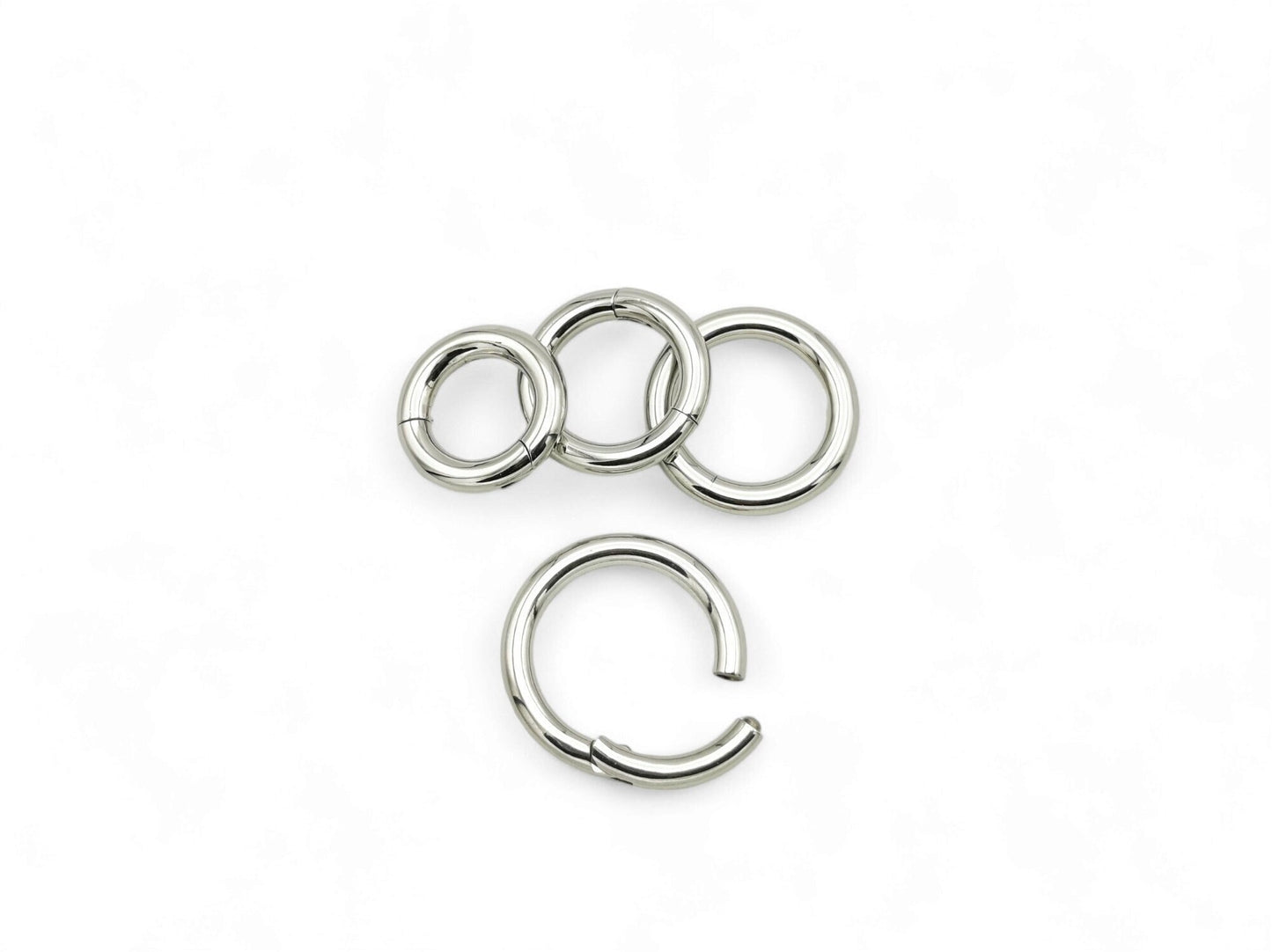 Three silver surgical steel clicker rings of different sizes arranged side by side against a white background.