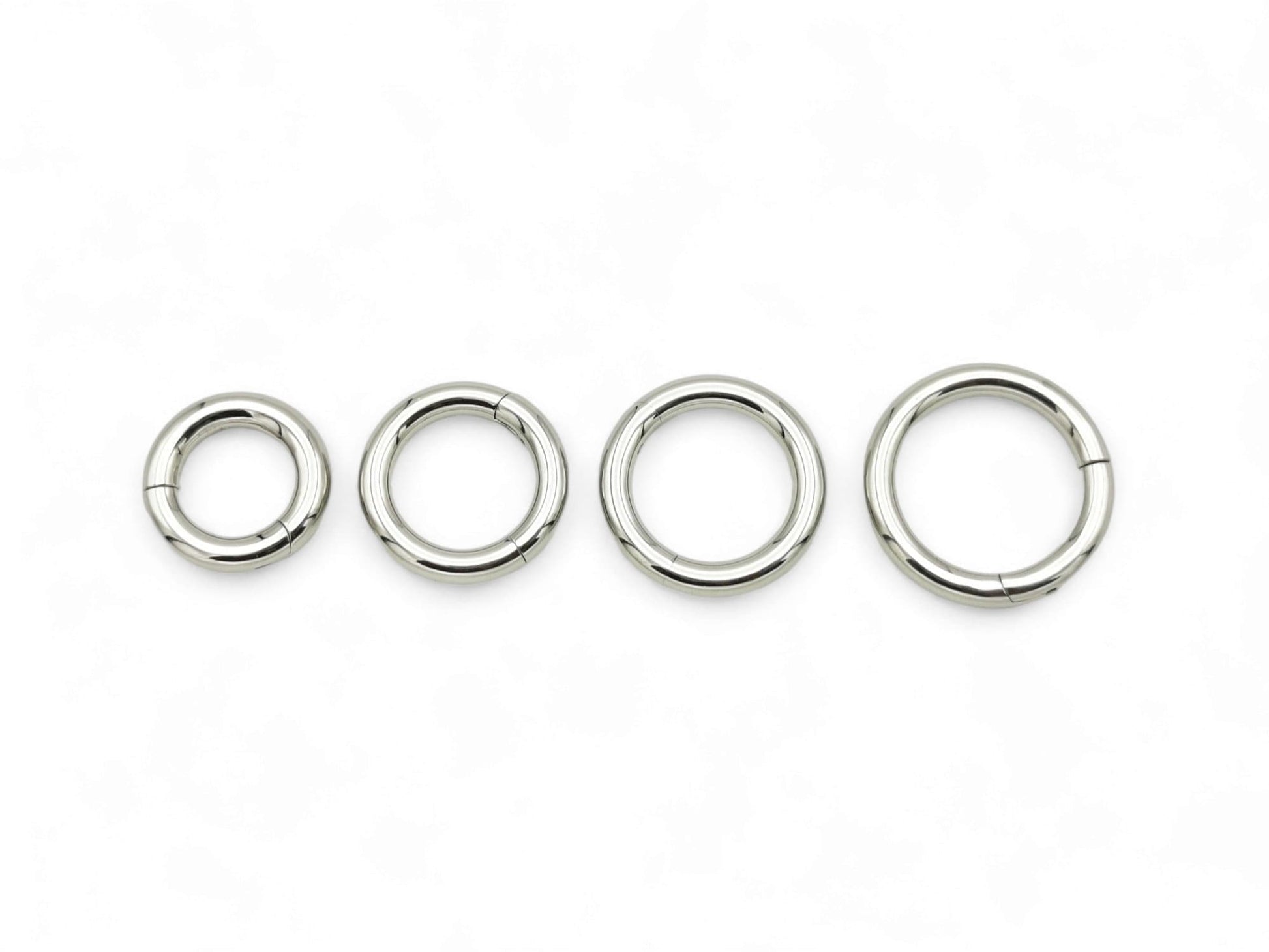 Three silver surgical steel clicker rings of different sizes arranged side by side against a white background.
