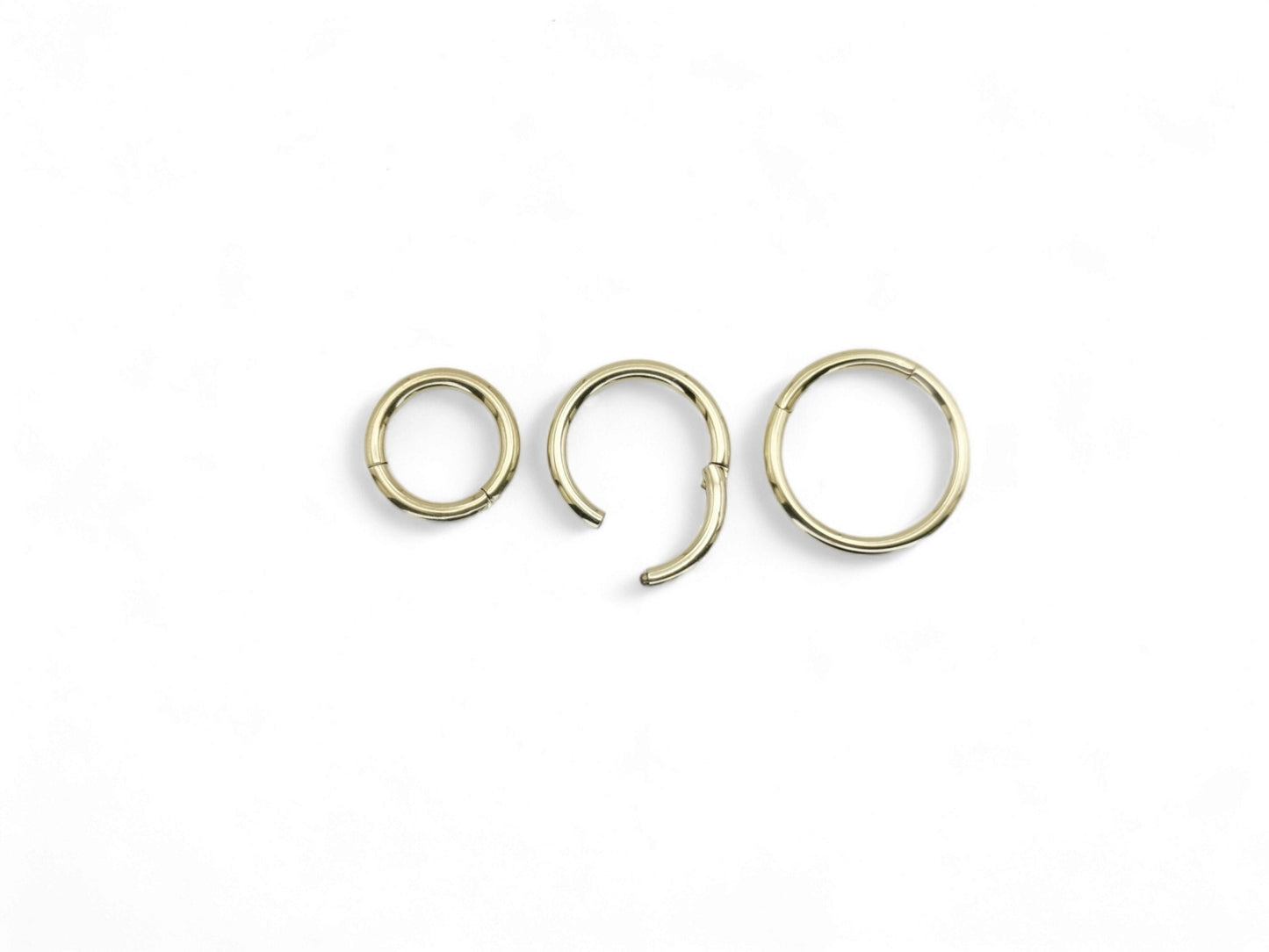 Three gold-colored surgical steel clicker rings for body piercings, displayed on a white background.