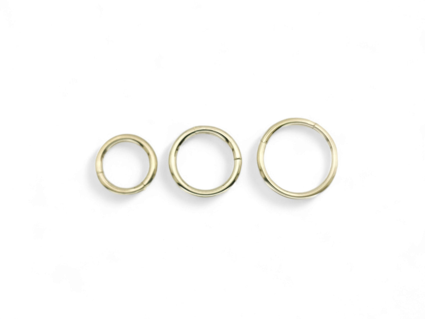 Three gold-colored surgical steel clicker rings for body piercings, displayed on a white background.