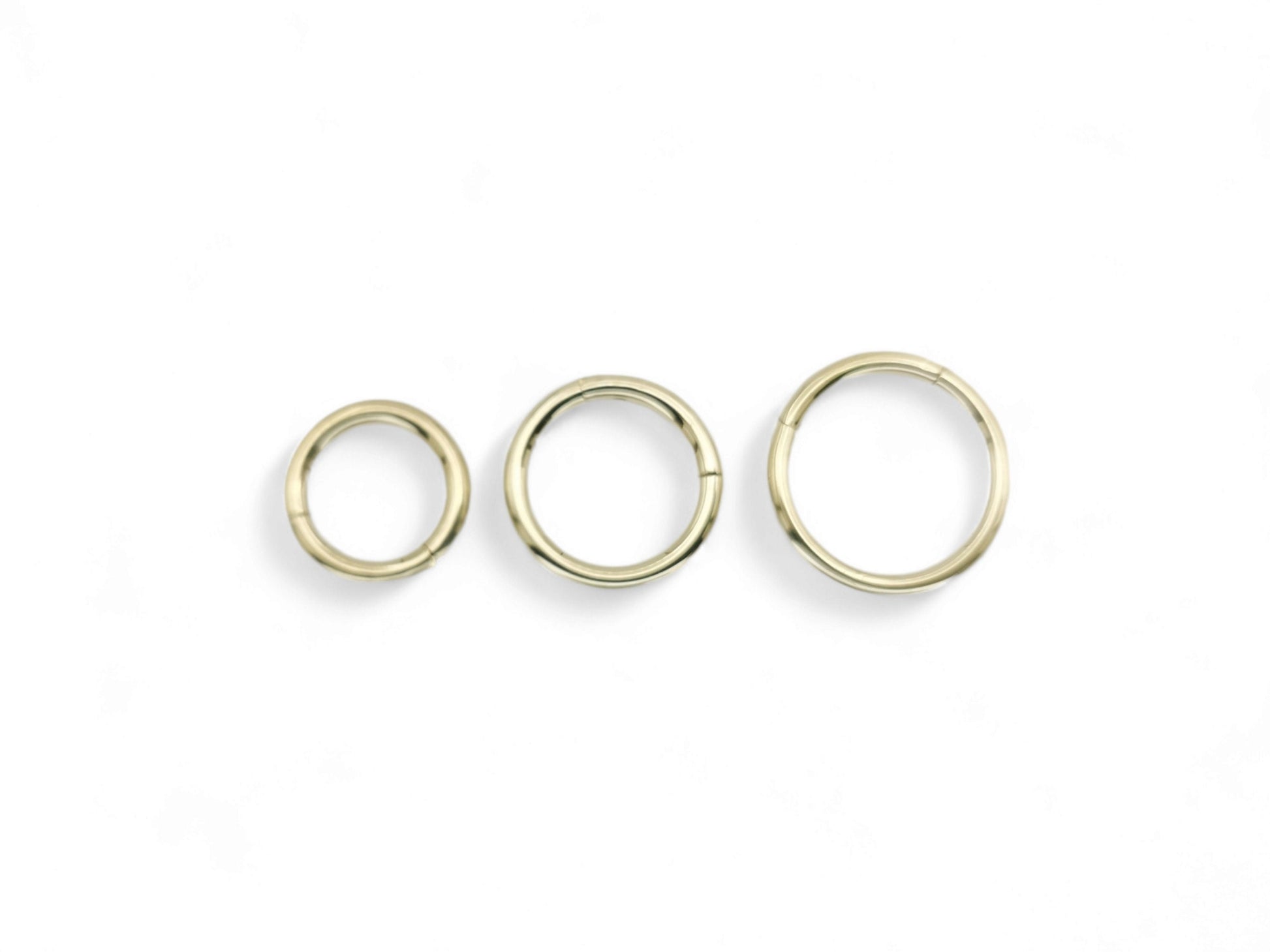 Three gold-colored surgical steel clicker rings for body piercings, displayed on a white background.
