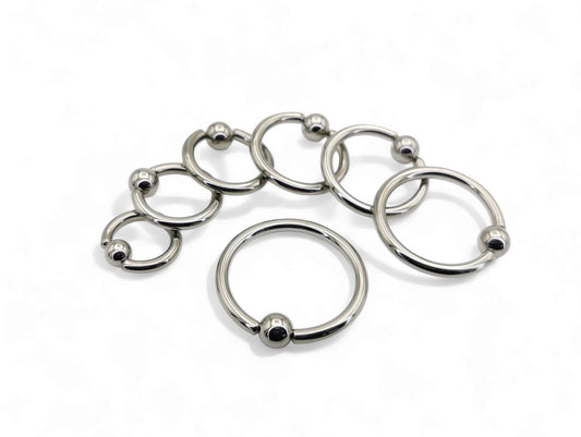 A collection of polished titanium BCRs with a ball/bead closure, displayed in two overlapping rows with varying diameters.