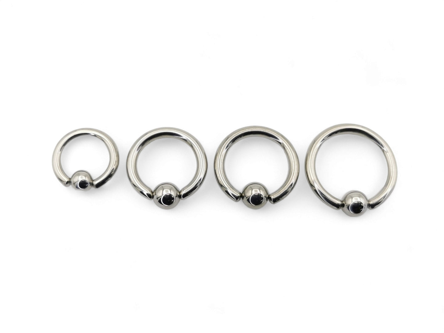 A collection of polished titanium BCRs with a ball/bead closure, displayed in two overlapping rows with varying diameters.