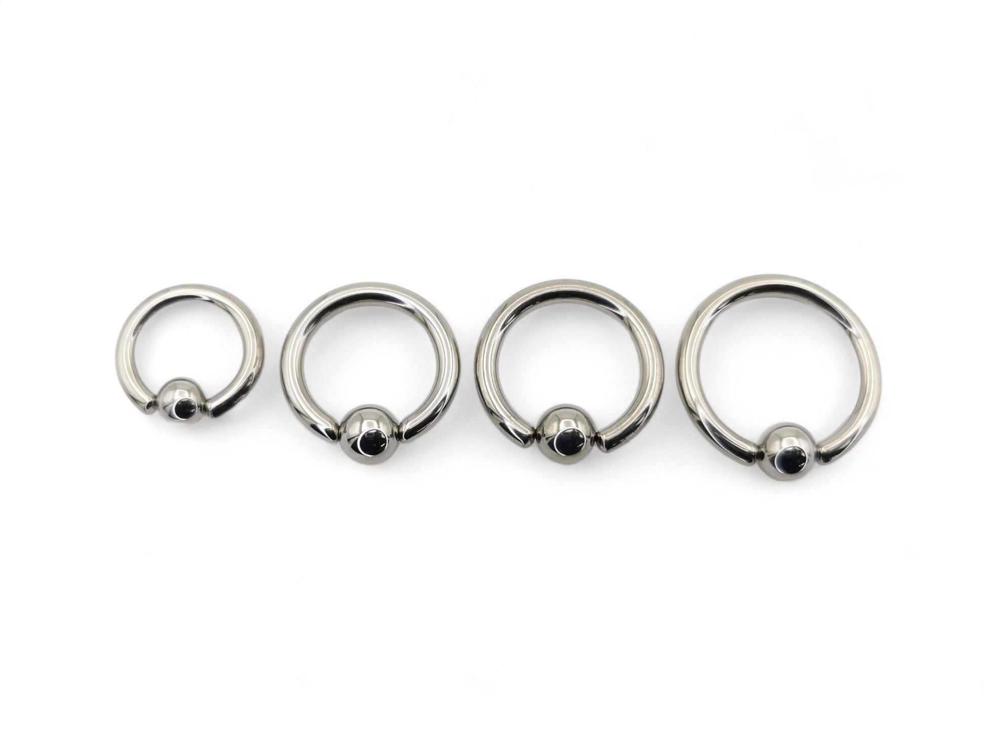 A collection of polished titanium BCRs with a ball/bead closure, displayed in two overlapping rows with varying diameters.