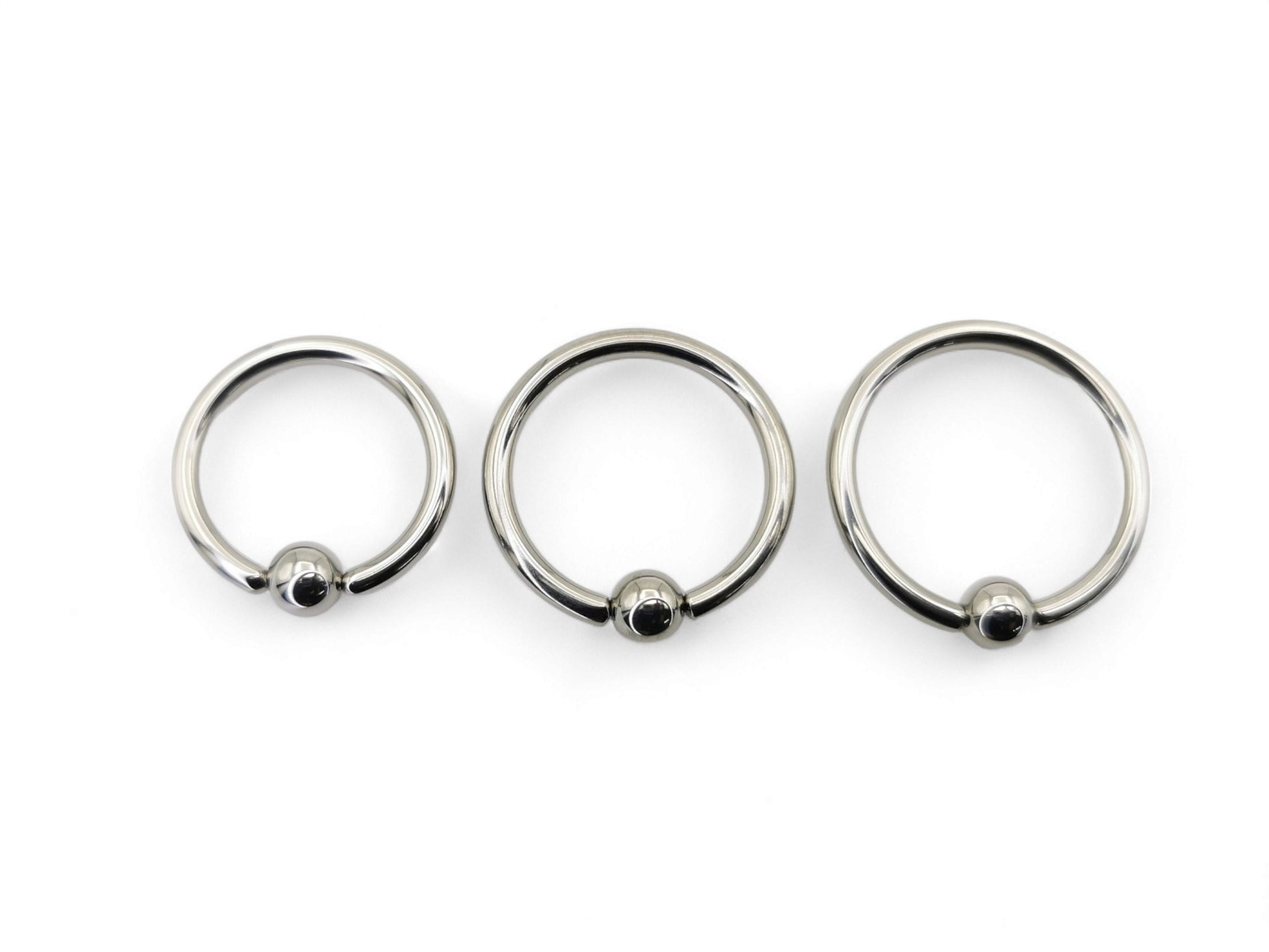 A collection of polished titanium BCRs with a ball/bead closure, displayed in two overlapping rows with varying diameters.
