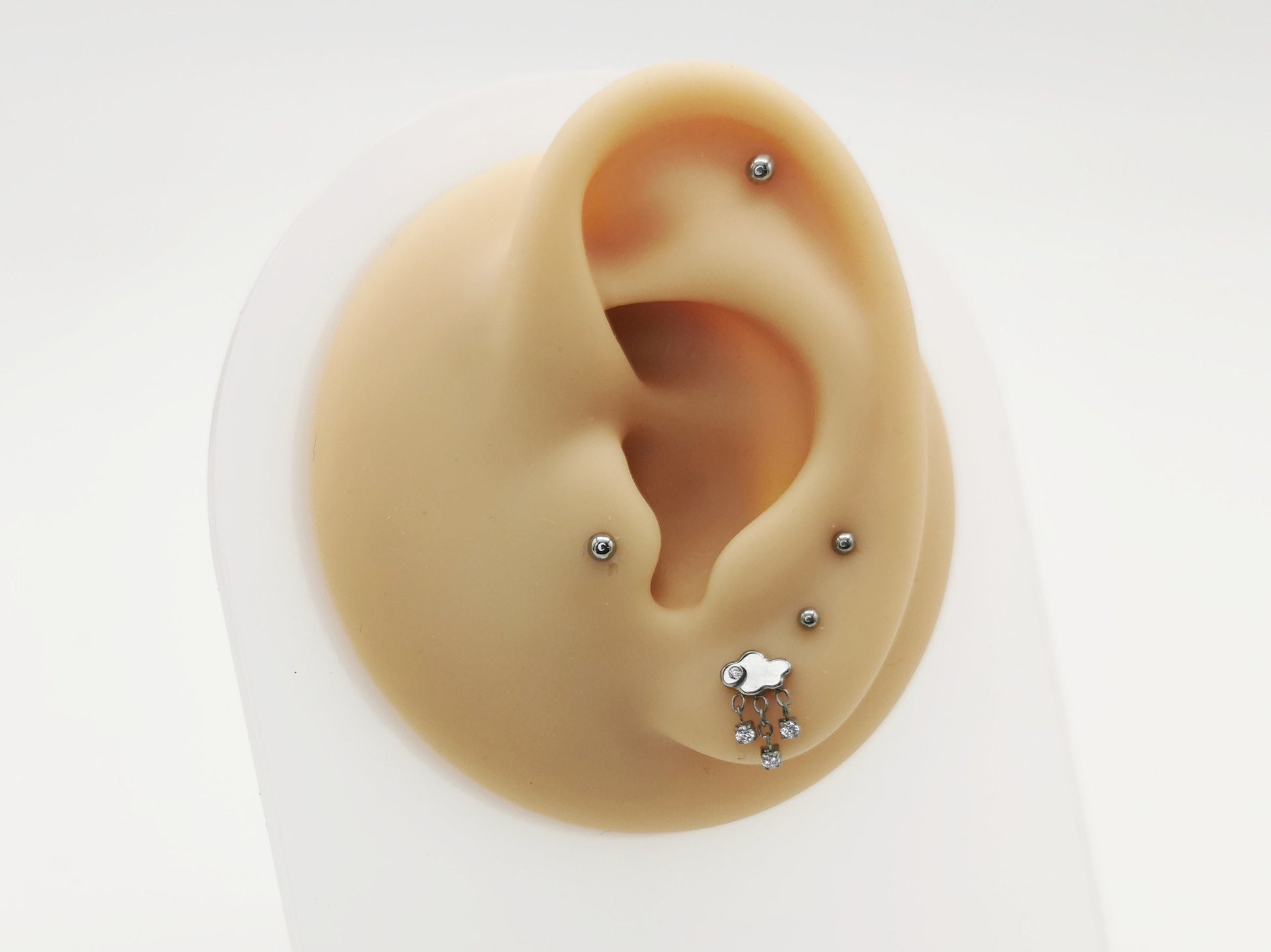 A silver-colored titanium threadless stud with a rain cloud shape and three jewelled rain drops, placed on a white background.