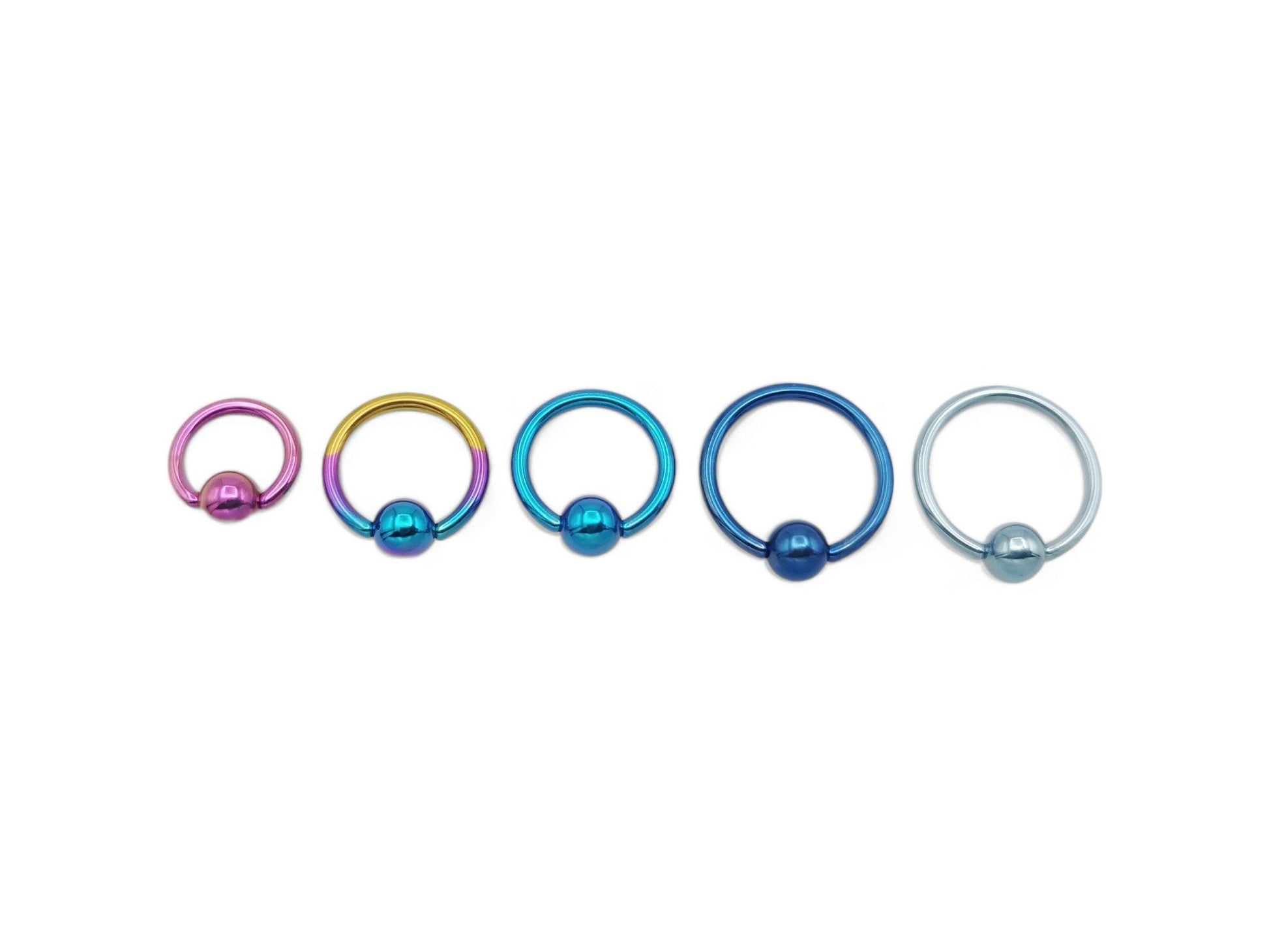 A set of five titanium anodized ball closure rings in different colors: blue, turquoise, pink, and a rainbow finish, with a shiny metallic appearance.