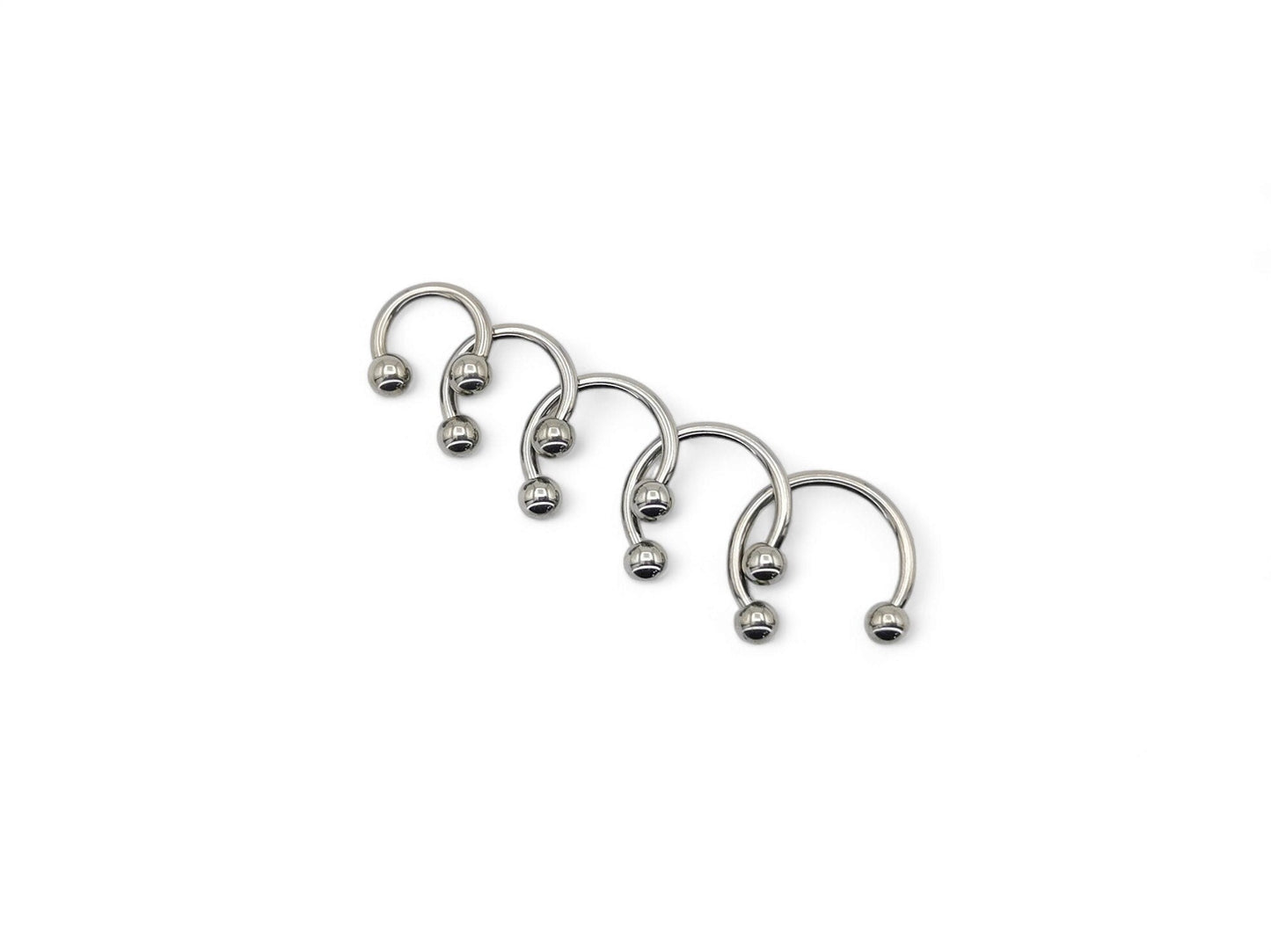 A collection of six titanium horseshoe barbells with a bright polished finish, arranged in a line against a white background.