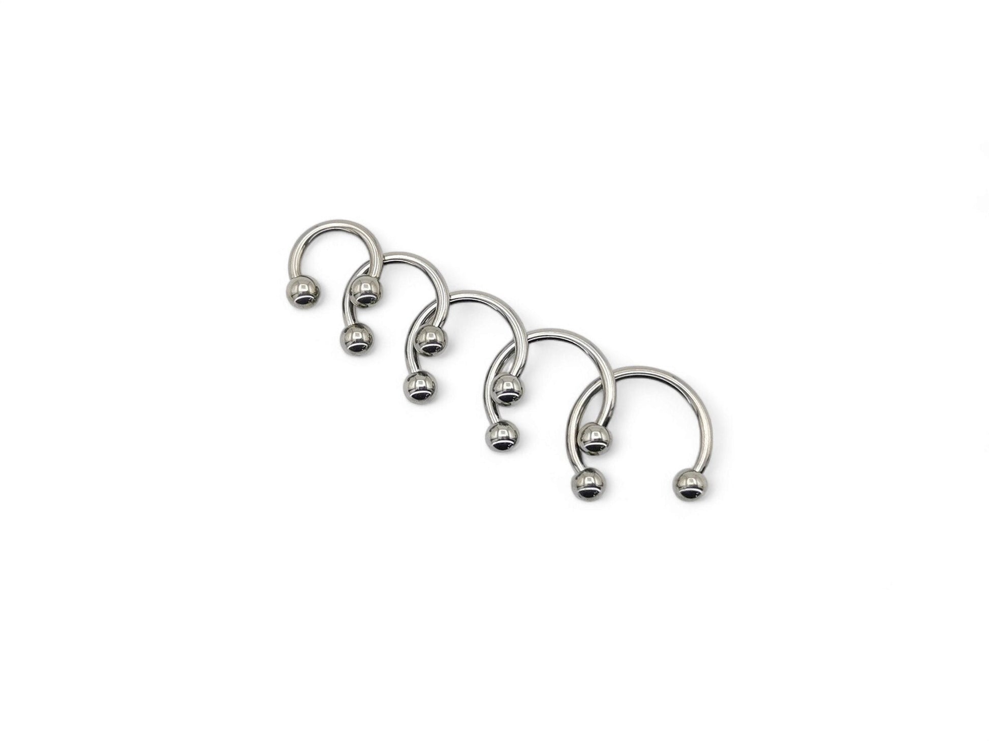 A collection of six titanium horseshoe barbells with a bright polished finish, arranged in a line against a white background.