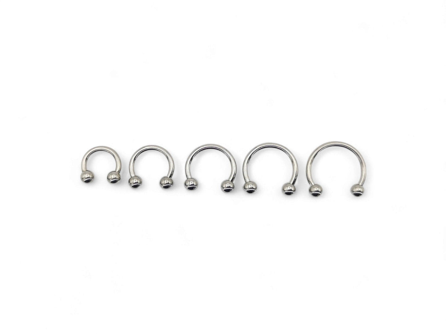 A collection of six titanium horseshoe barbells with a bright polished finish, arranged in a line against a white background.