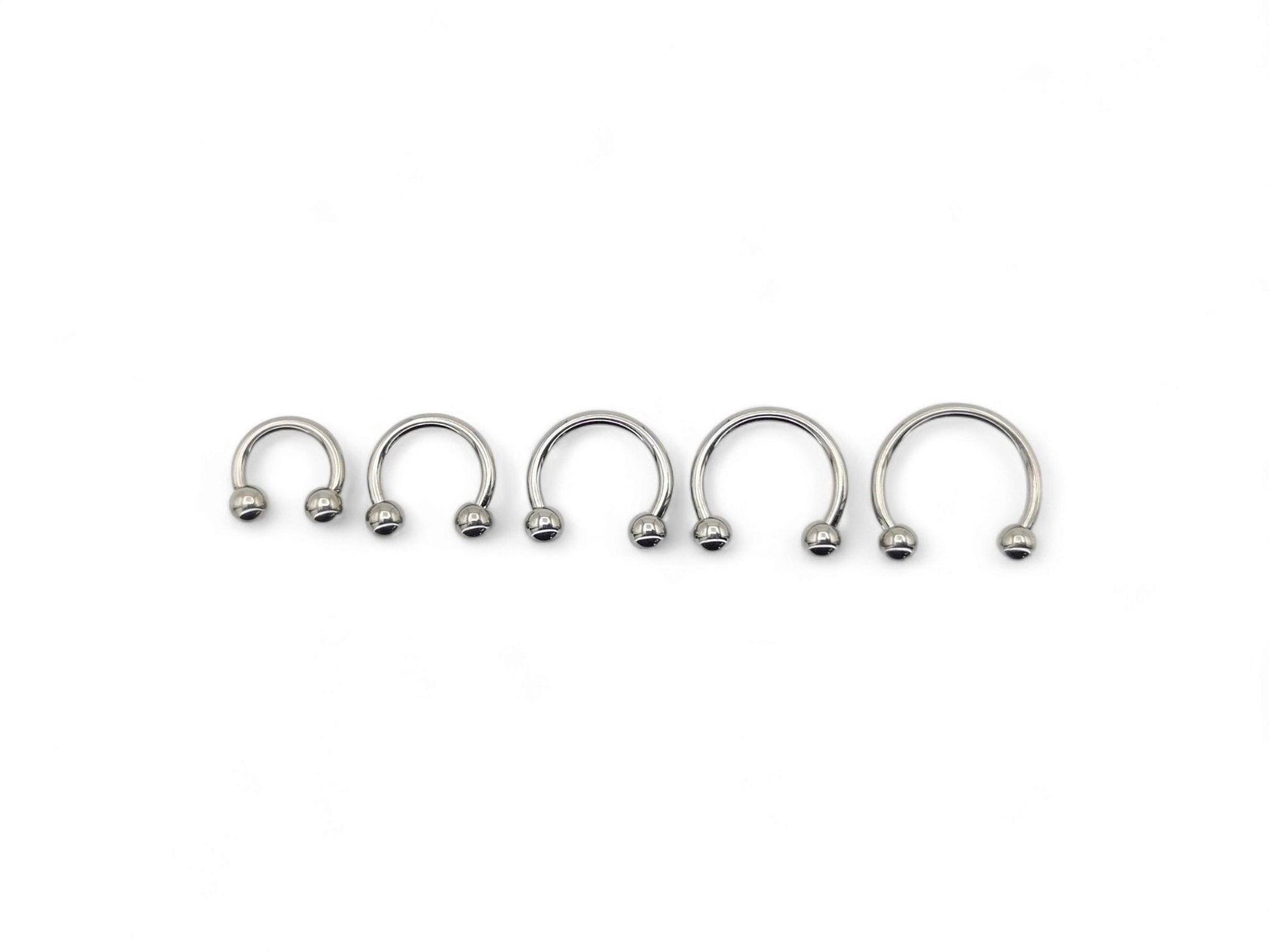 A collection of six titanium horseshoe barbells with a bright polished finish, arranged in a line against a white background.