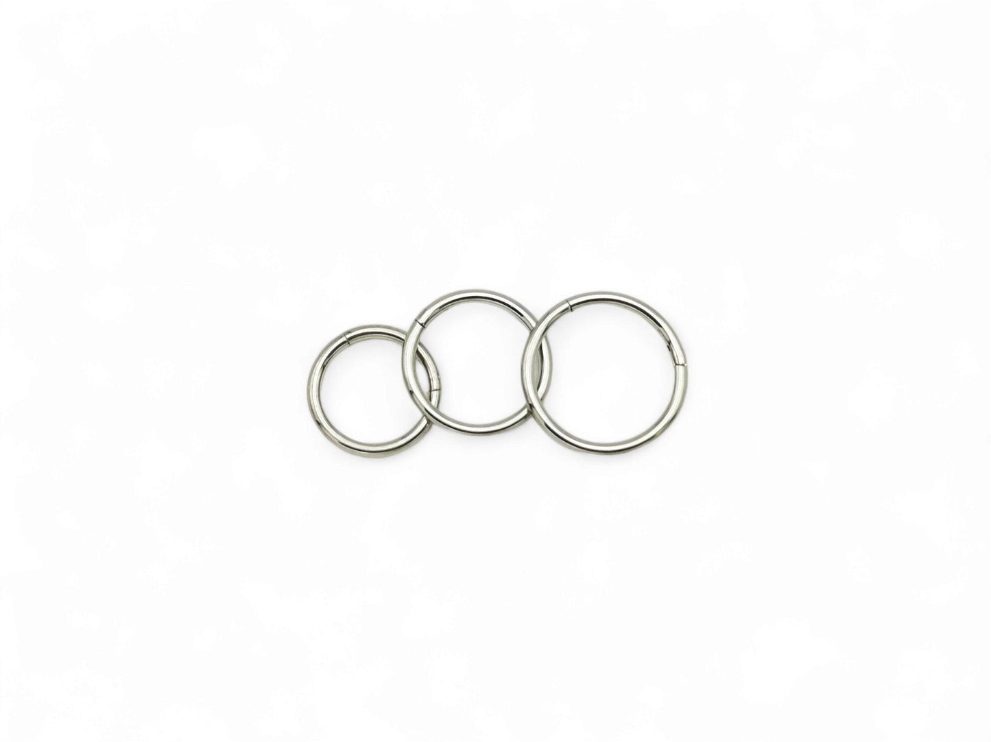 Three overlapping titanium clicker rings with a polished finish, arranged in a stacked configuration against a white background.